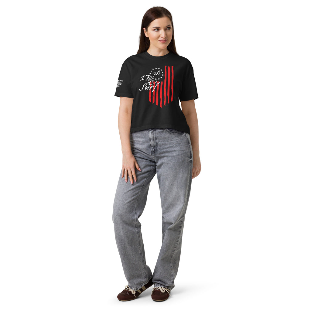 Woman wearing the black "1776 & Surf" boxy tee, front view, featuring the large 1776 script logo with 13-star Betsy Ross flag and distressed red stripe graphic – America's 250th Anniversary Collection by 17th & Surf