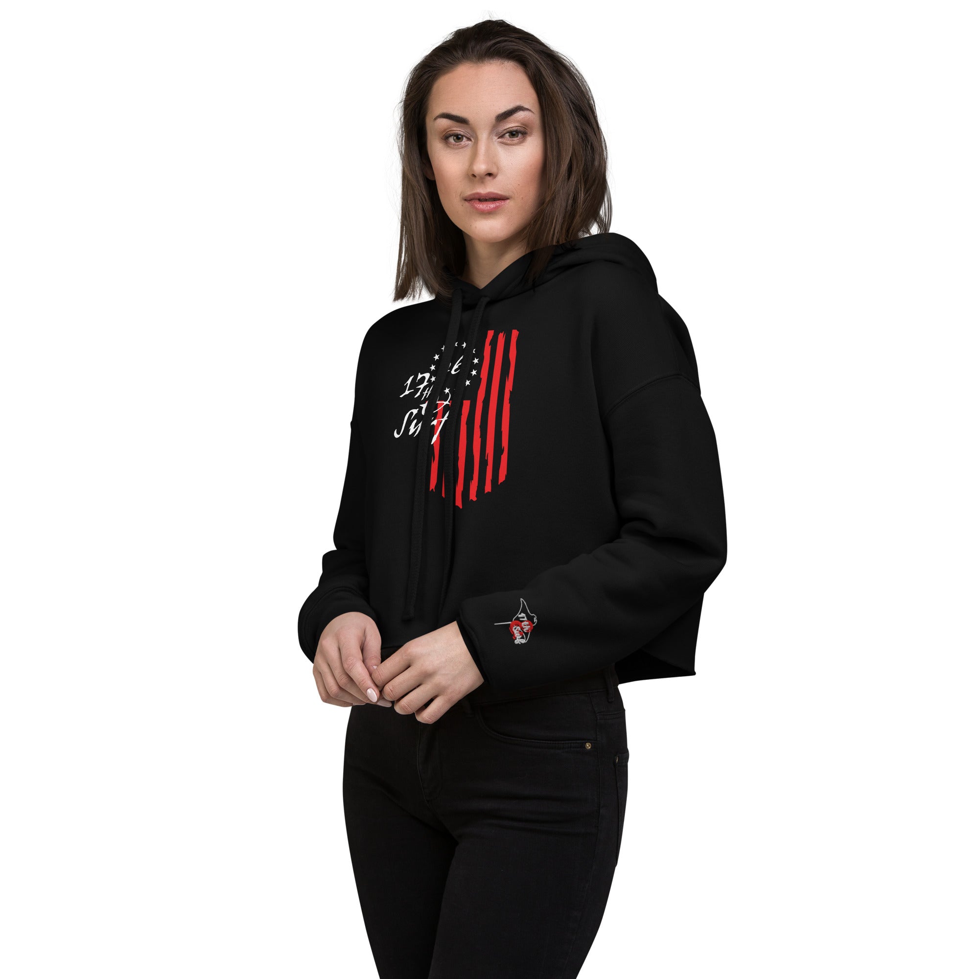 Woman wearing the black "1776 & Surf" crop hoodie, angled front view, showing the 1776 script logo with 13-star Betsy Ross flag graphic and the embroidered '17th & Surf' logo on the sleeve cuff – America's 250th Anniversary Collection by 17th & Surf