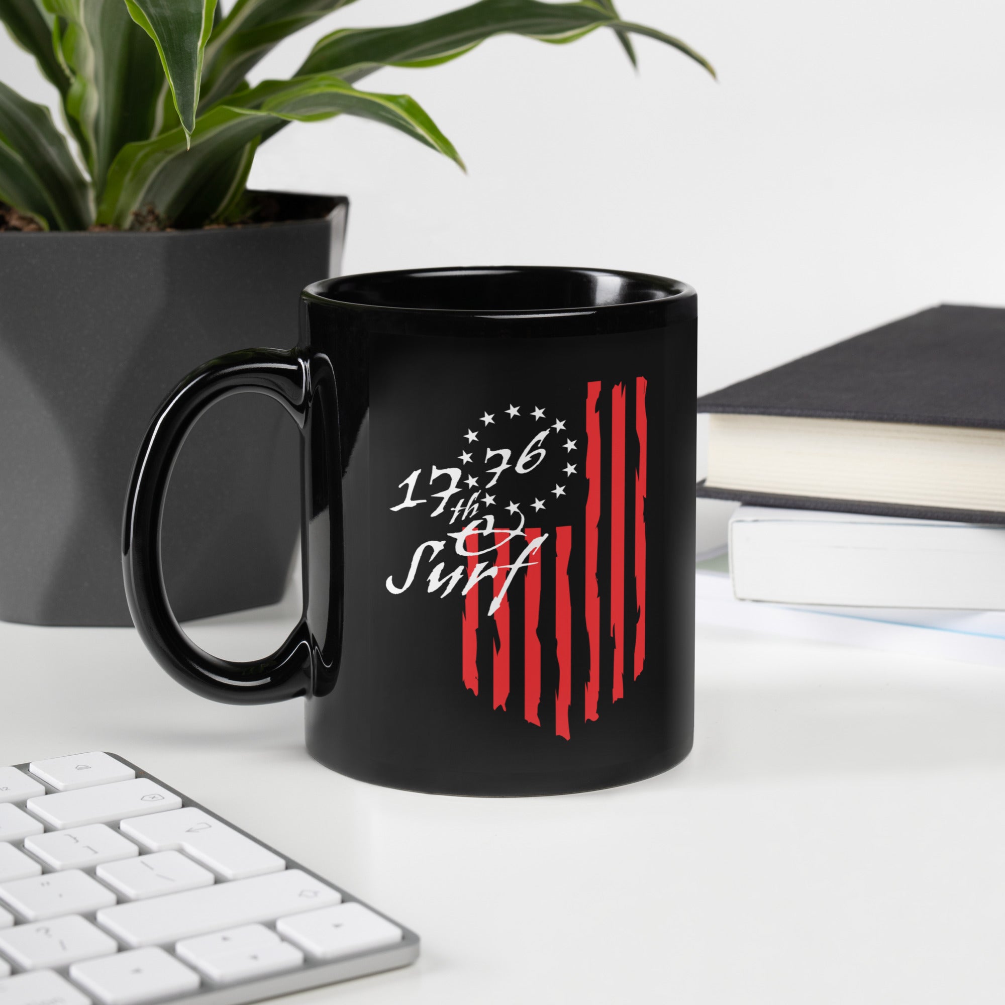 Black 1776 & Surf coffee mug on a desk with plants, books, and a keyboard, featuring the 1776 script logo and 13-star Betsy Ross flag design – America's 250th Anniversary Collection by 17th & Surf