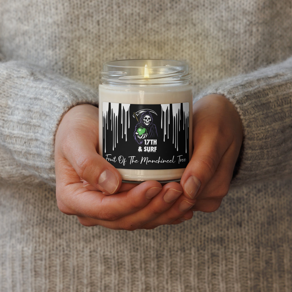 "Fruit Of The Manchineel Tree" 9oz scented soy candle lit and held in hands featuring Grim Reaper holding green apple label with "17th & Surf" logo – "Beach Apple" Series by 17th & Surf
