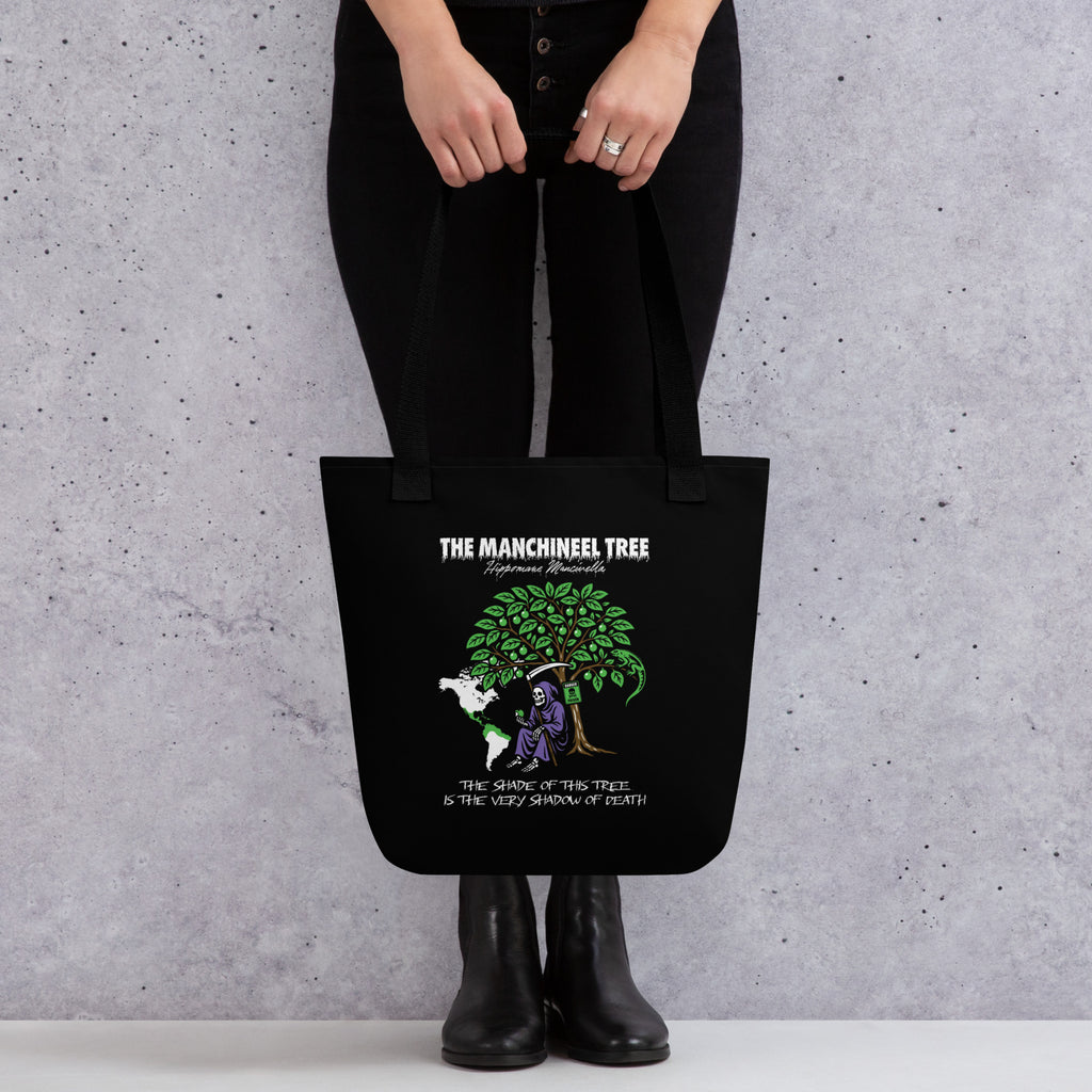 "Beach Apple" black canvas tote bag, front view on model, featuring the large "THE MANCHINEEL TREE" graphic with the Grim Reaper, green iguana, "DANGER POISON" sign, and map of Central/South America – "Beach Apple" Series by 17th & Surf