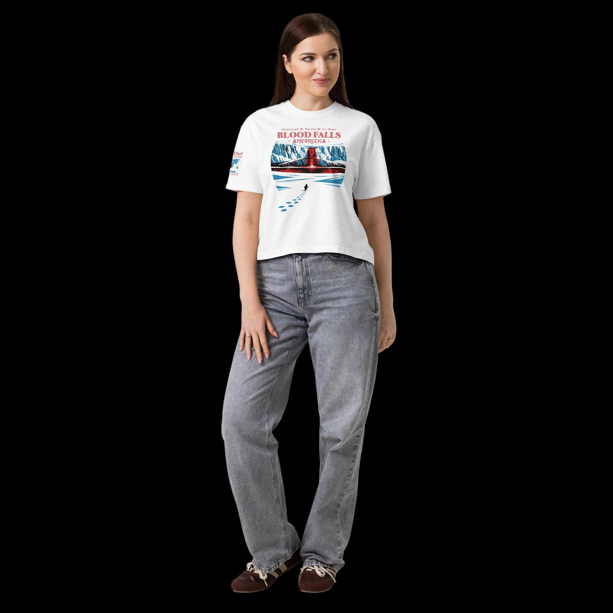 Full-body model wearing white women’s heavyweight boxy t-shirt with Blood Falls Antarctica design with lone penguin approaching the red waterfall and haunted seas sleeve patch