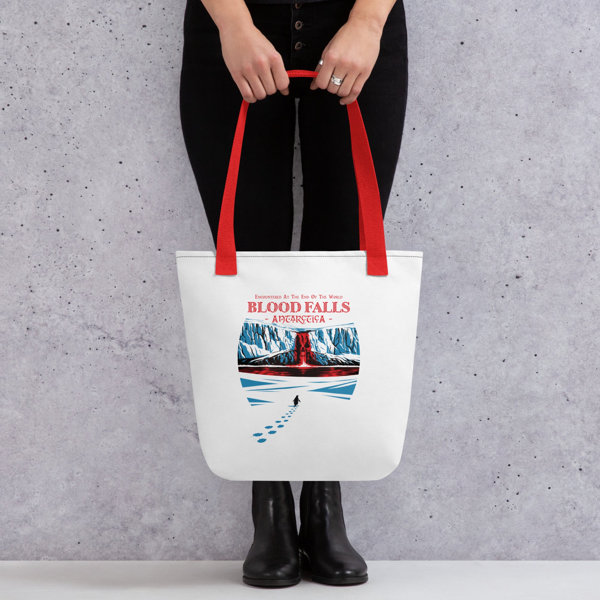"Blood Falls" Antarctica tote bag, held by model showing front panel, featuring a crimson waterfall cascading from the Taylor Glacier ice cliffs with a lone nihilist penguin walking toward the falls – Haunted Seas Series by 17th & Surf