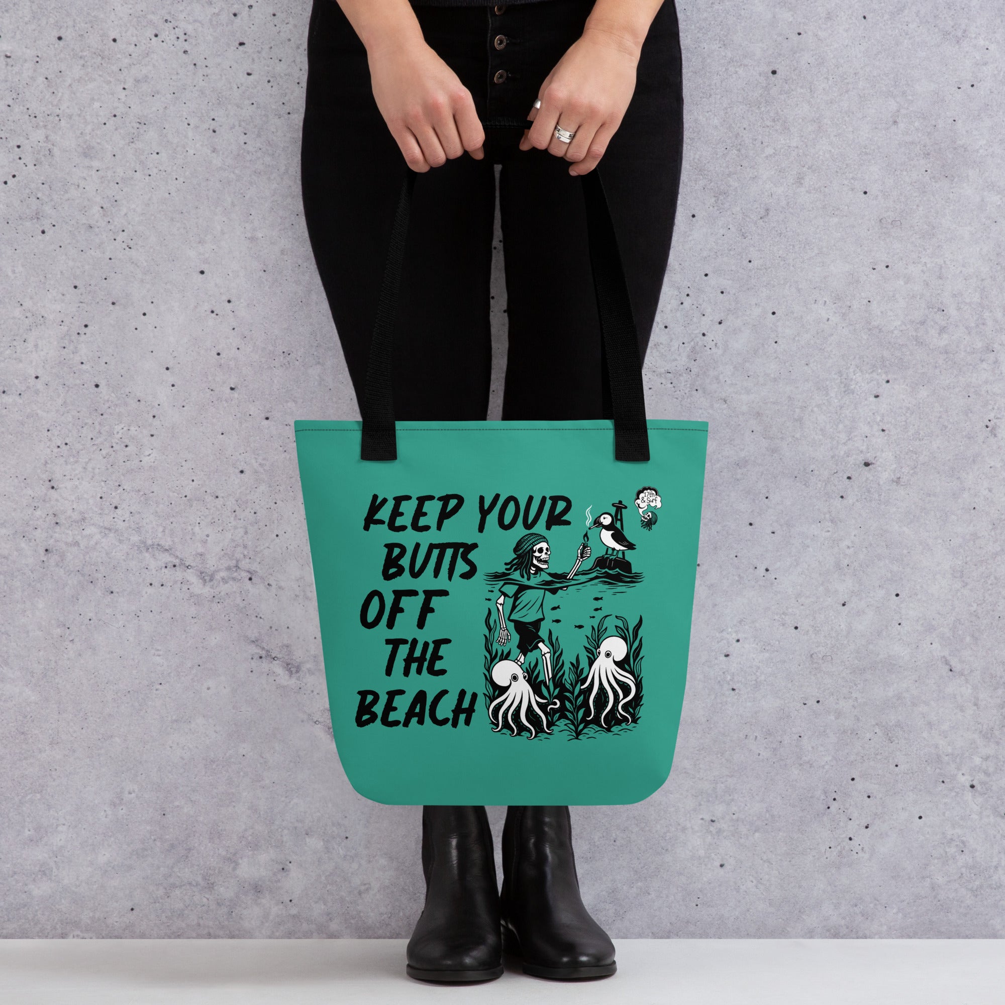 "Keep Your Butts Off The Beach" teal canvas tote bag held by model featuring skeleton lighting a cigarette for a puffin with octopuses in seaweed and "Keep Your Butts Off The Beach" text graphic - 17th & Surf