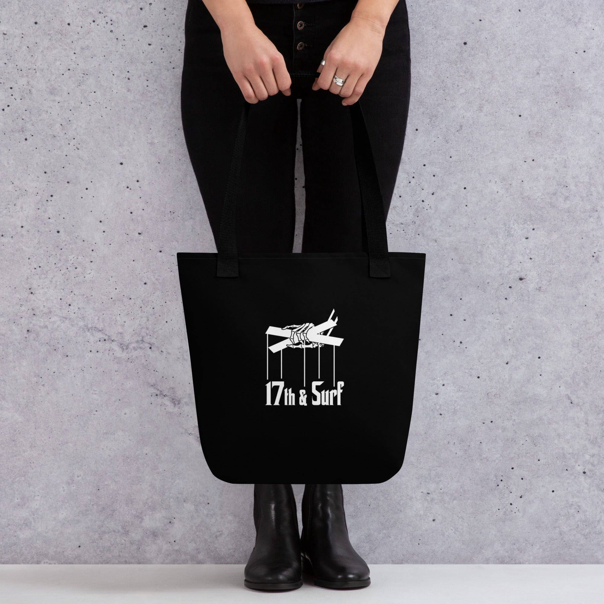 Woman holding the "Clams Casino" black canvas tote bag, back view, featuring the small "17th & Surf" skeletal puppeteer-hand logo – Clam's Casino Series by 17th & Surf