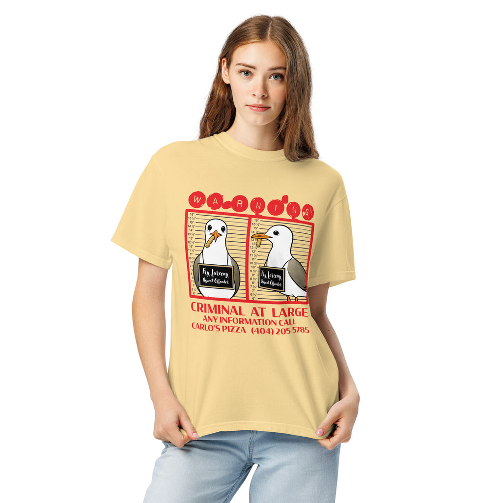 "Criminal At Large" pale yellow garment-dyed heavyweight tee on female model, front view, featuring seagull "WARNING" mugshot graphic with "Fry Larceny, Repeat Offender" police lineup – 17th & Surf x Carlo's Pizza