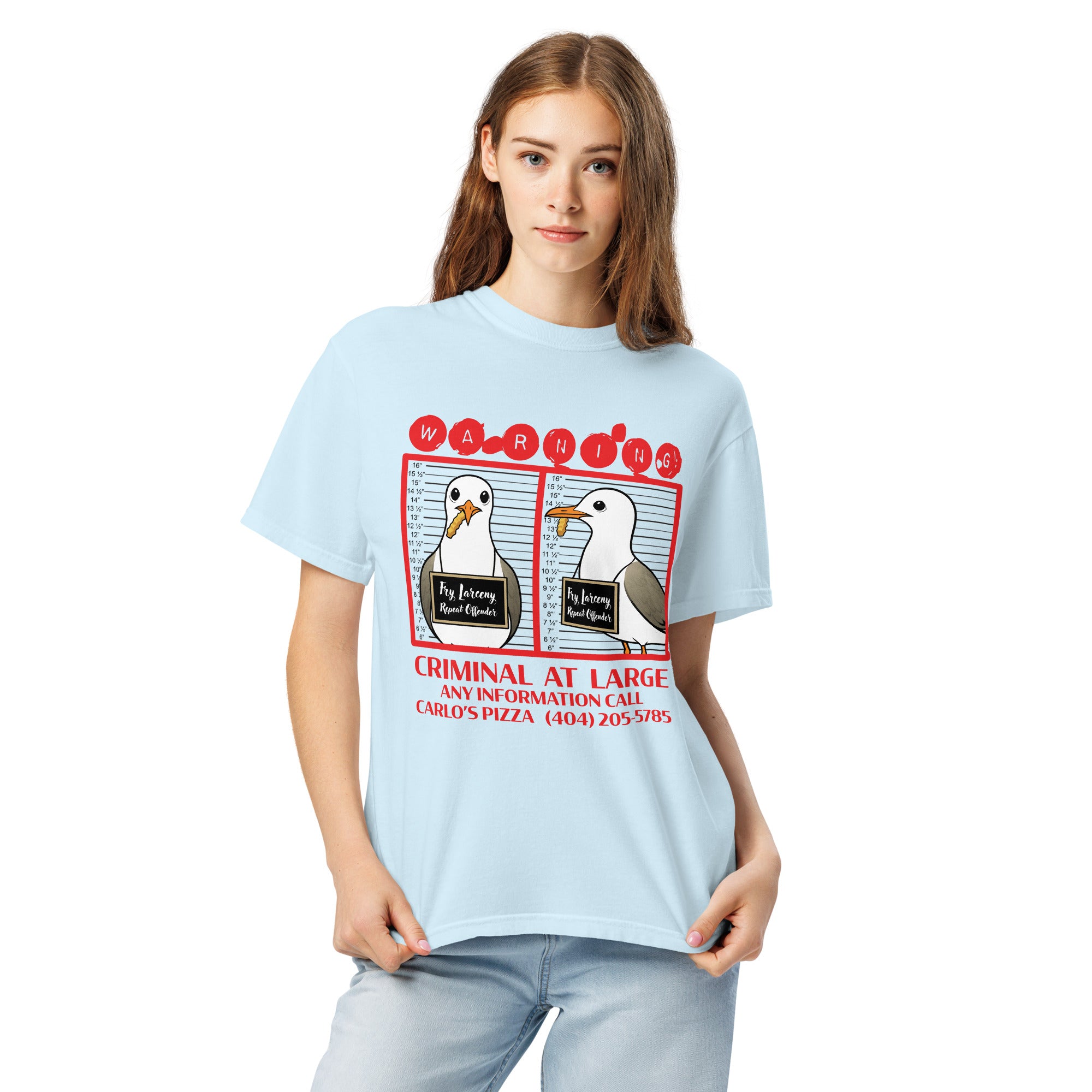 "Criminal At Large" light blue garment-dyed heavyweight tee on female model, front view, featuring seagull "WARNING" mugshot graphic with "Fry Larceny, Repeat Offender" police lineup – 17th & Surf x Carlo's Pizza