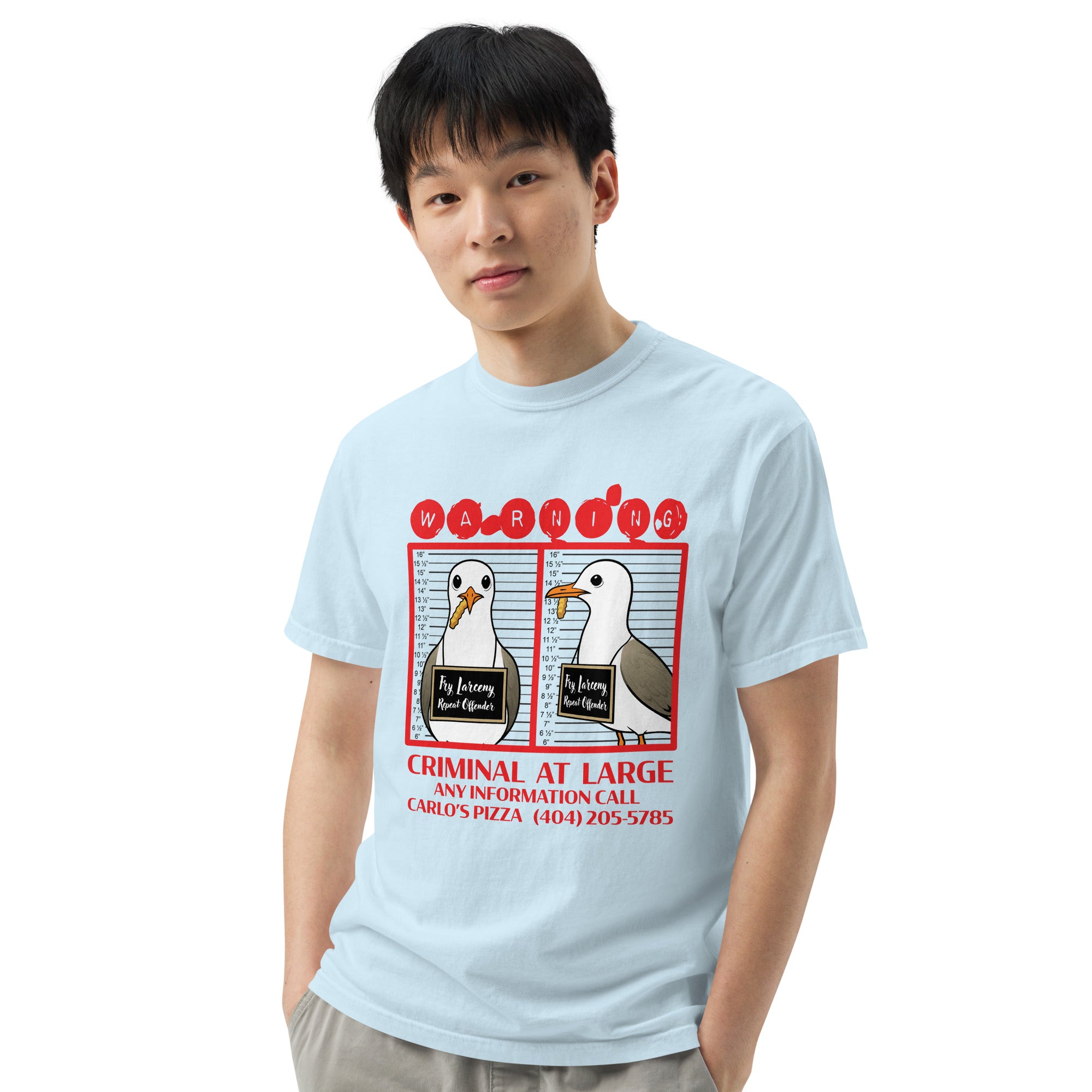 "Criminal At Large" light blue garment-dyed heavyweight tee on male model, front view, featuring seagull "WARNING" mugshot graphic with "Fry Larceny, Repeat Offender" police lineup – 17th & Surf x Carlo's Pizza