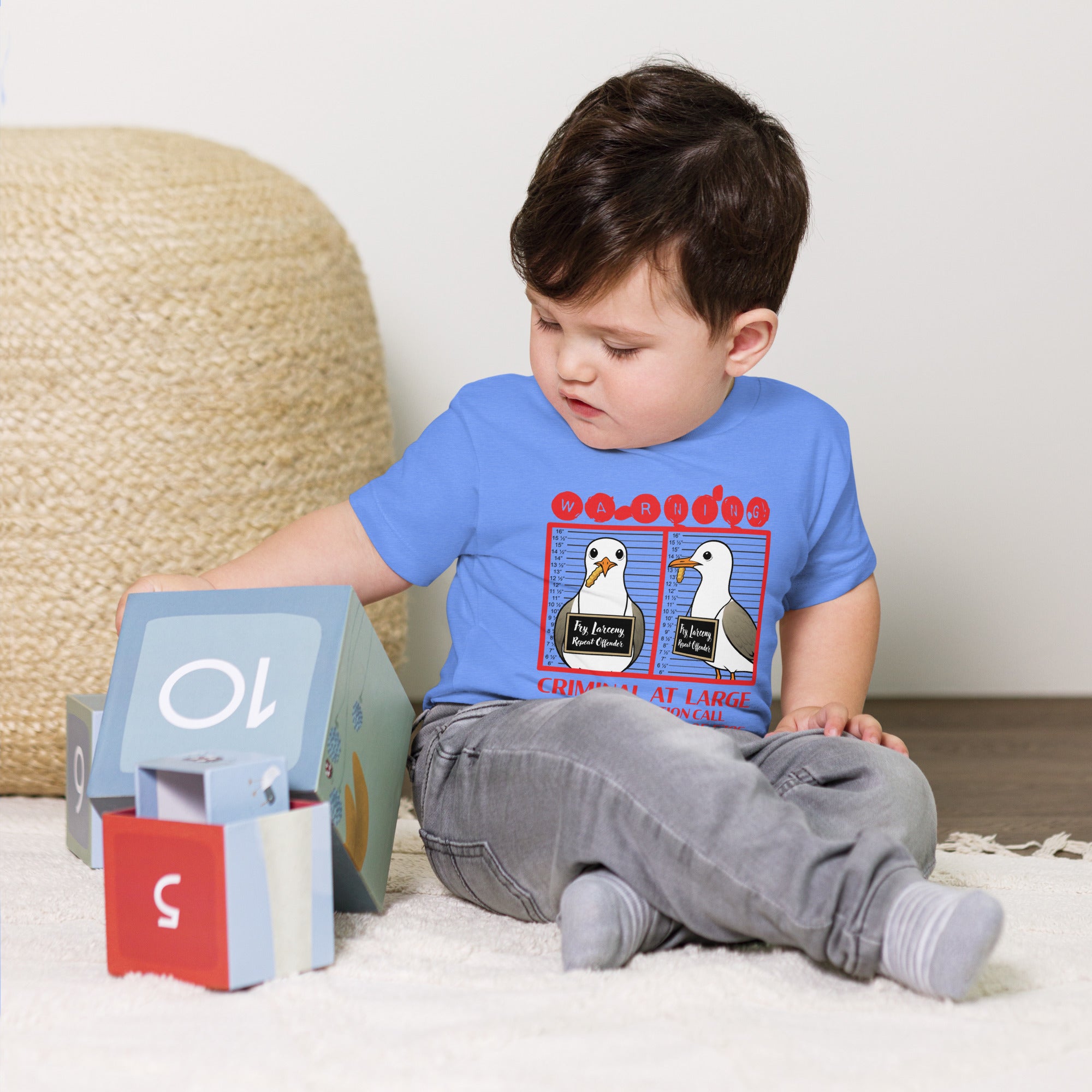 "Criminal At Large" columbia blue toddler tee on toddler model, front view, featuring seagull "WARNING" mugshot graphic with "Fry Larceny, Repeat Offender" police lineup – 17th & Surf x Carlo's Pizza