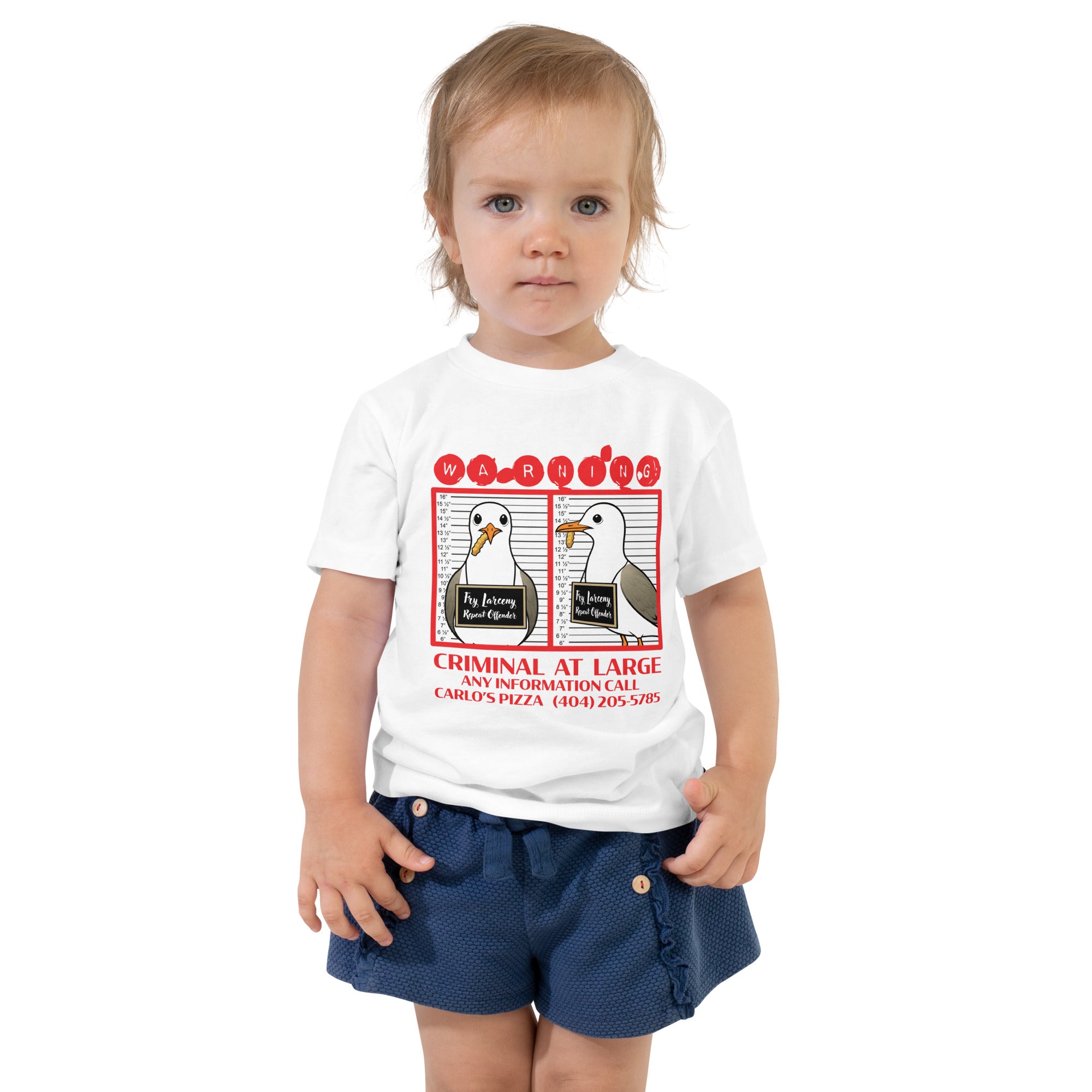 "Criminal At Large" white toddler tee on toddler model, front view, featuring seagull "WARNING" mugshot graphic with "Fry Larceny, Repeat Offender" police lineup – 17th & Surf x Carlo's Pizza