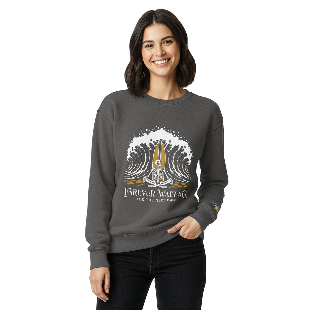 "Forever Waiting For The Next Wave" crewneck sweatshirt, Pepper, third front view, featuring a meditating skeleton surfer, board planted upright behind him, sitting cross-legged on the shore as breakers roll in on either side – 17th & Surf