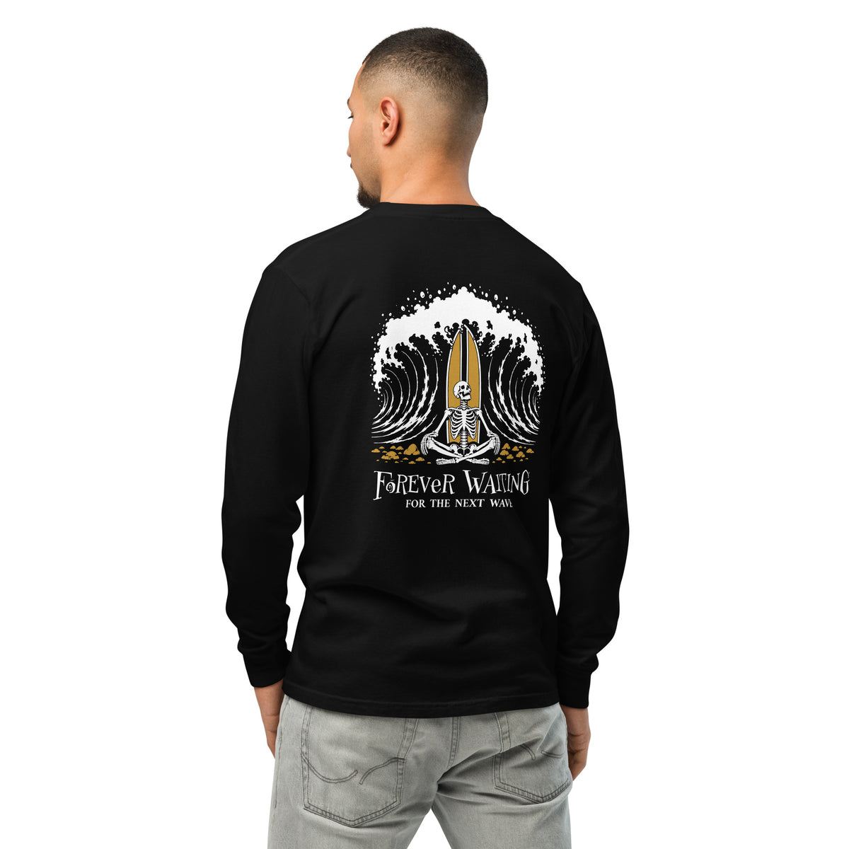 "Forever Waiting For The Next Wave" long sleeve shirt, Black, third back view, featuring a meditating skeleton surfer, board planted upright behind him, sitting cross-legged on the shore as breakers roll in on either side – 17th & Surf