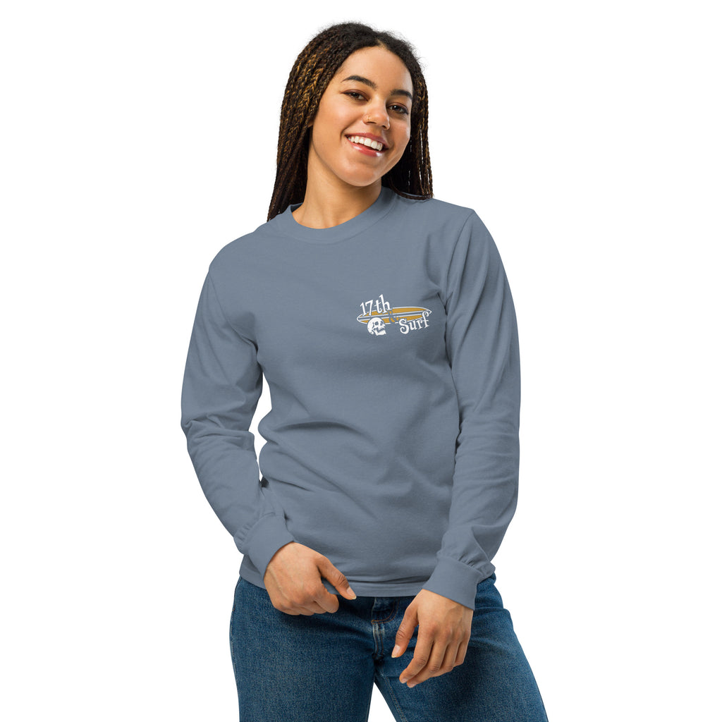 "Forever Waiting For The Next Wave" long sleeve shirt, Blue Jean, second front view, featuring a meditating skeleton surfer, board planted upright behind him, sitting cross-legged on the shore as breakers roll in on either side – 17th & Surf