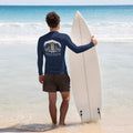"Forever Waiting For The Next Wave" rash guard, back view, featuring a meditating skeleton surfer, board planted upright behind him, sitting cross-legged on the shore as breakers roll in on either side – 17th & Surf