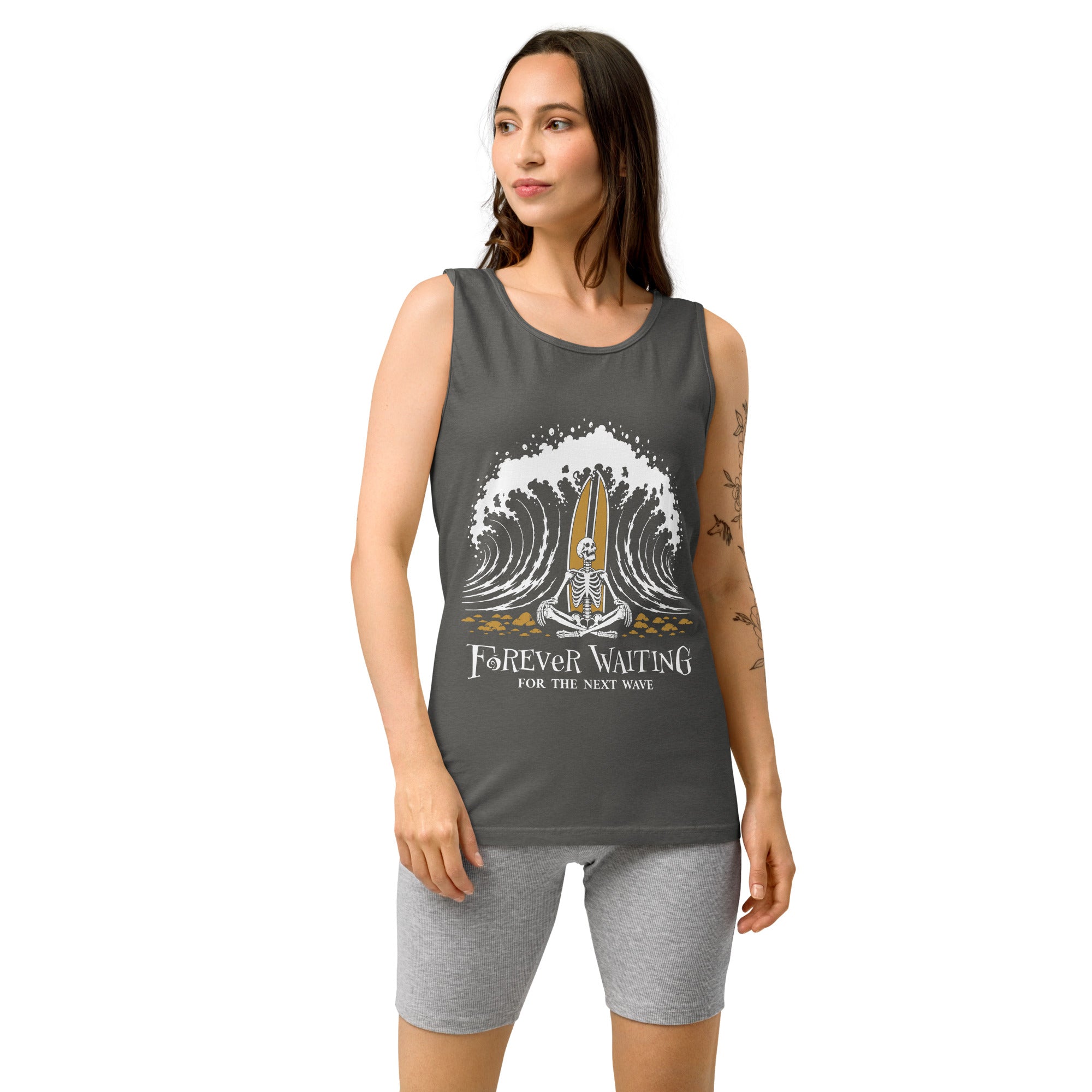 "Forever Waiting For The Next Wave" tank top, Pepper, third front view, featuring a meditating skeleton surfer, board planted upright behind him, sitting cross-legged on the shore as breakers roll in on either side – 17th & Surf