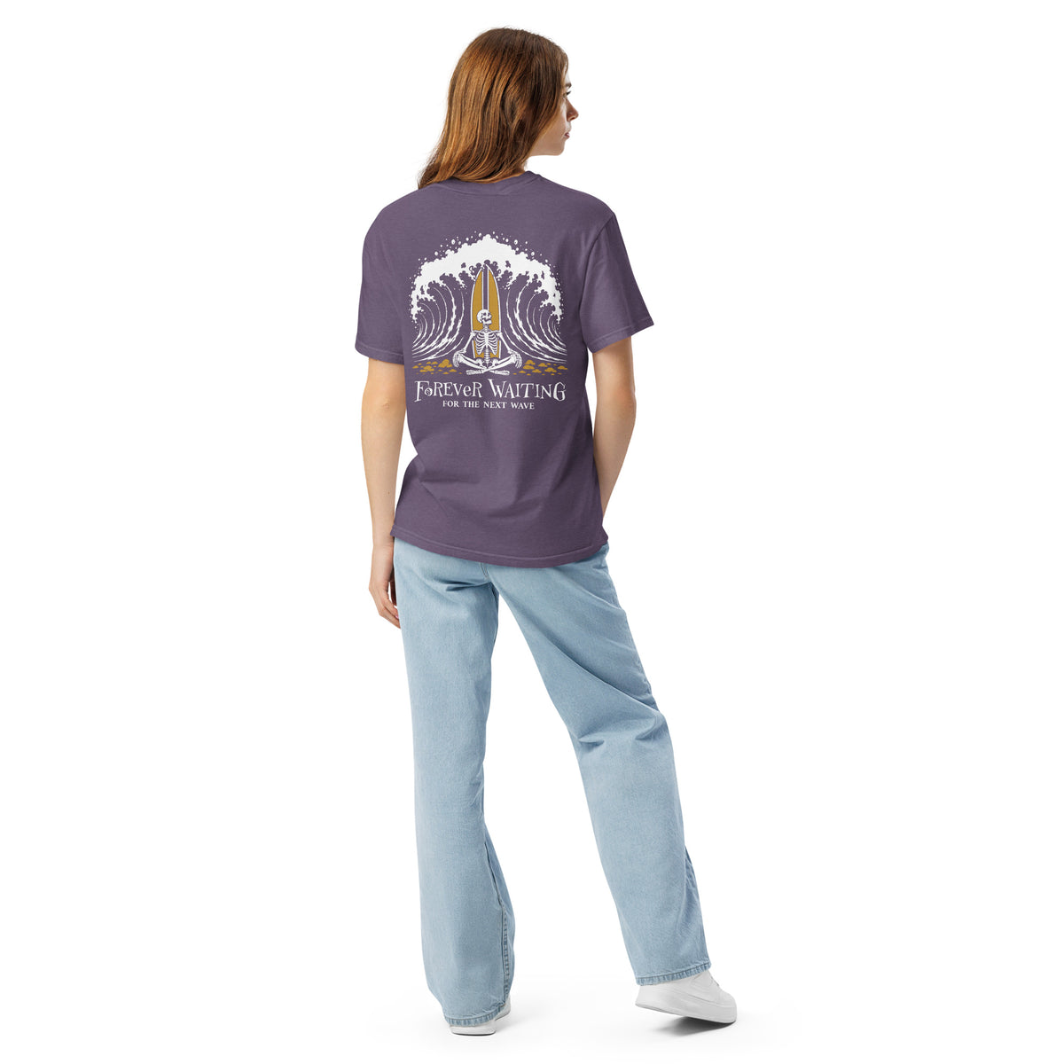 "Forever Waiting For The Next Wave" tee, Grape, second back view, featuring a meditating skeleton surfer, board planted upright behind him, sitting cross-legged on the shore as breakers roll in on either side – 17th & Surf
