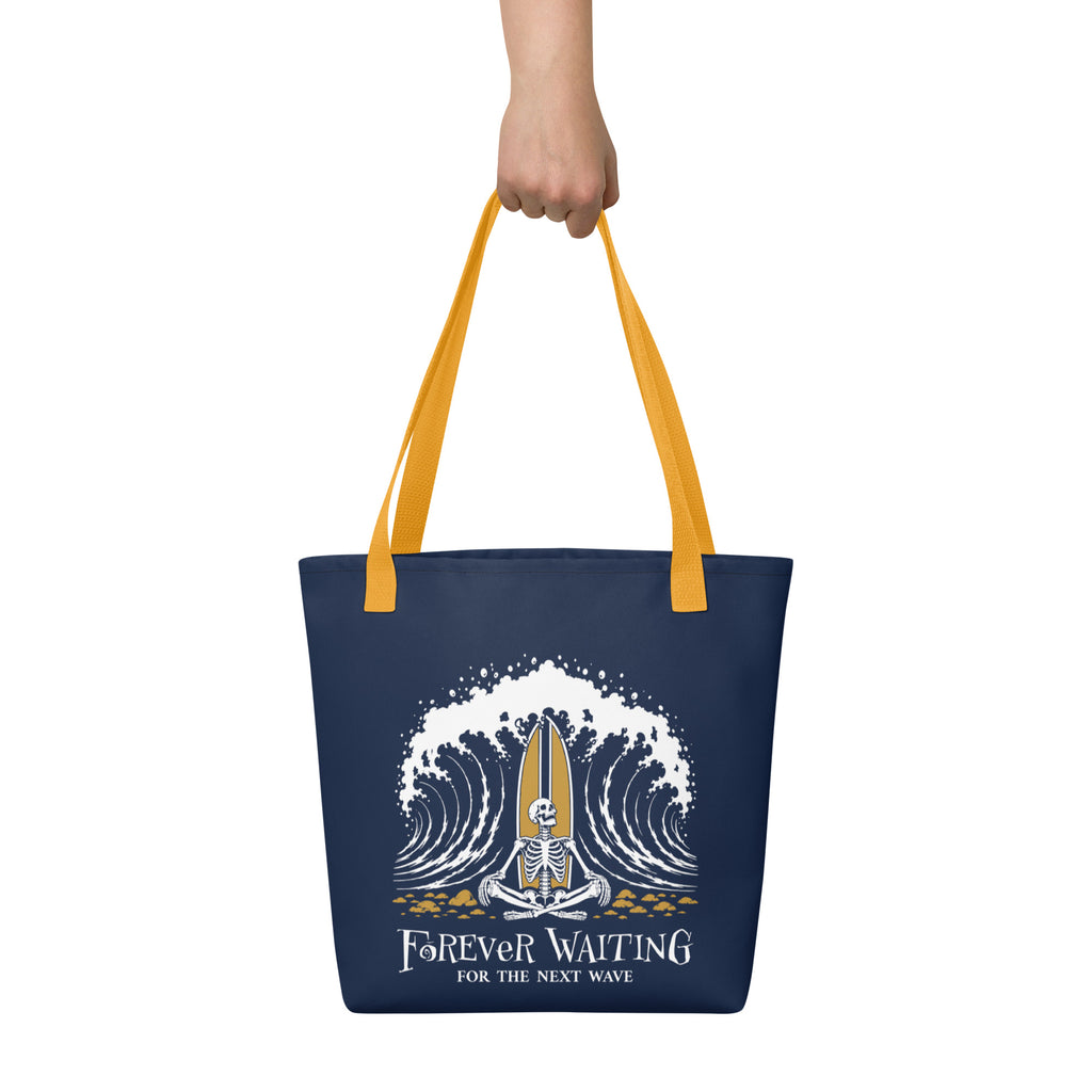 "Forever Waiting For The Next Wave" tote bag, front view, featuring a meditating skeleton surfer, board planted upright behind him, sitting cross-legged on the shore as breakers roll in on either side – 17th & Surf