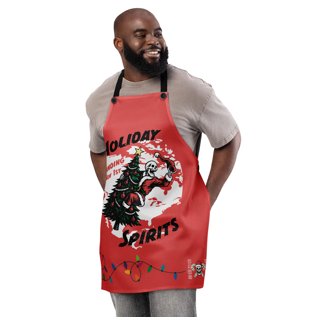 "Holiday Spirits" chef apron in white, front view featuring full color graphic of a skeleton Santa riding a decorated Christmas tree inside a white splatter map shape with arched "Holiday" and "Spirits" text, a string of colorful Christmas lights along the hem, and small "17th & Surf" candy cane crossbones skull logo – 17th & Surf