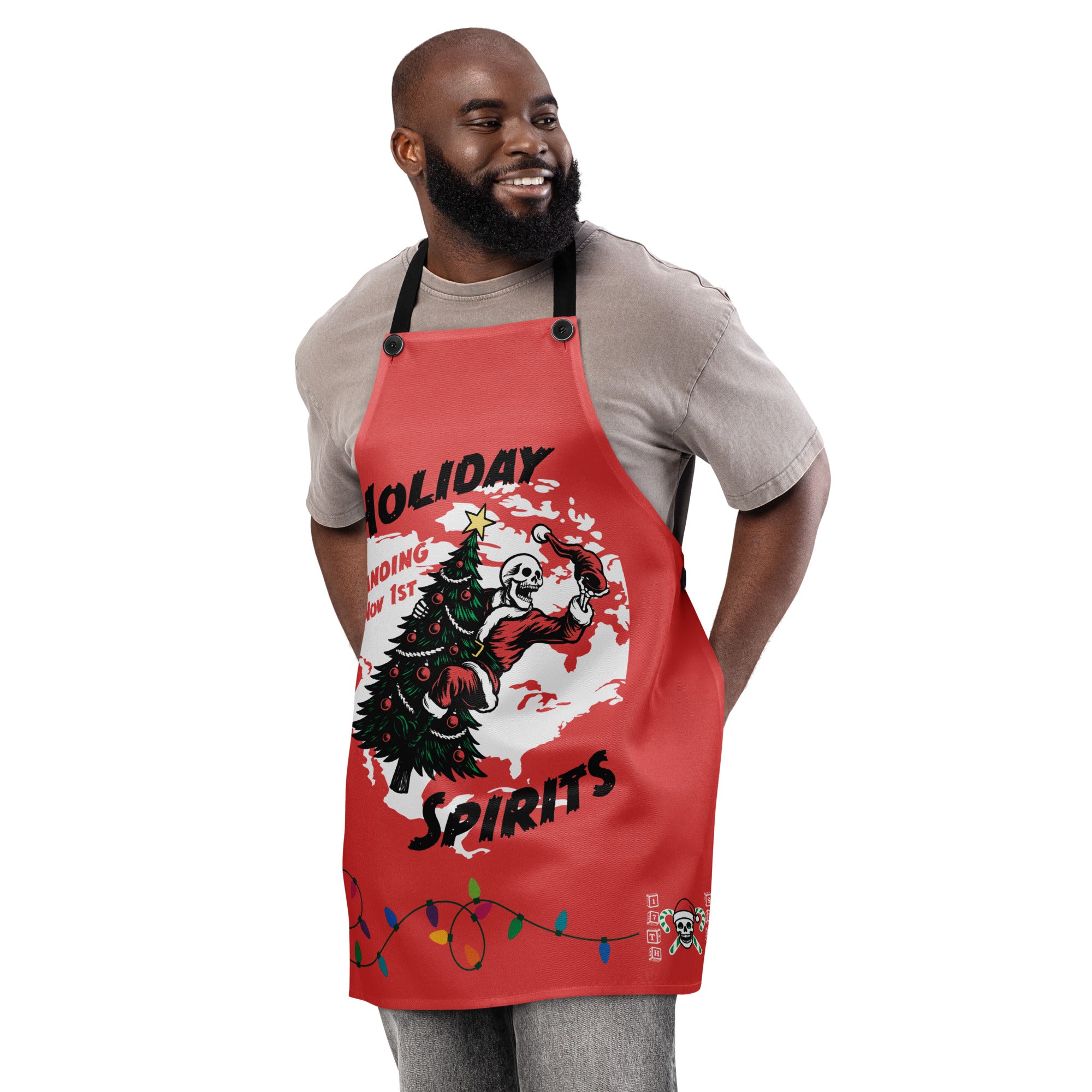 "Holiday Spirits" chef apron in white, front view featuring full color graphic of a skeleton Santa riding a decorated Christmas tree inside a white splatter map shape with arched "Holiday" and "Spirits" text, a string of colorful Christmas lights along the hem, and small "17th & Surf" candy cane crossbones skull logo – 17th & Surf