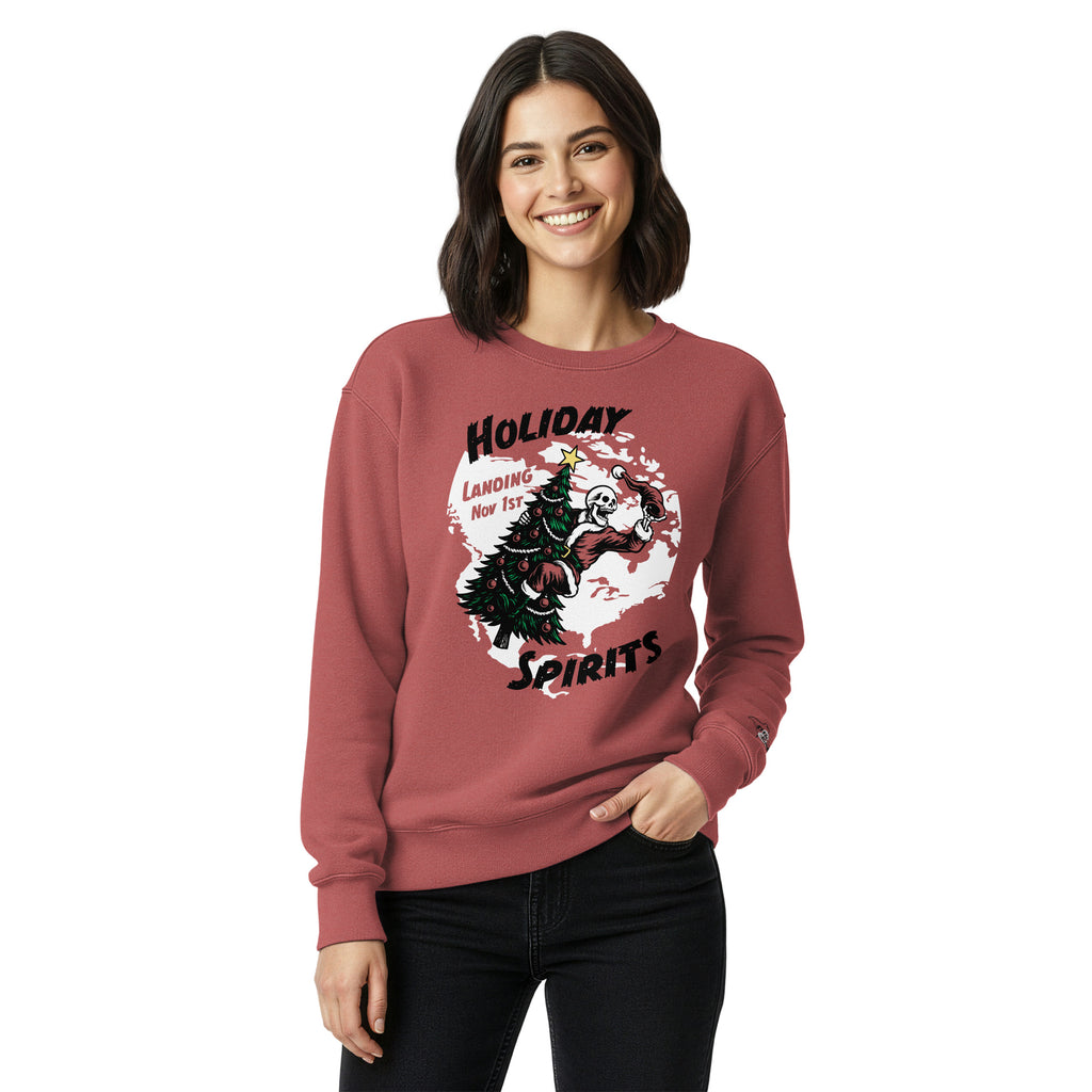 Model wearing "Holiday Spirits" heavyweight crewneck sweatshirt in crimson red, second front view featuring full color graphic of a skeleton Santa riding a decorated Christmas tree inside a white splatter map shape with arched "Holiday" and "Spirits" text and "Landing Nov 1st" – 17th & Surf