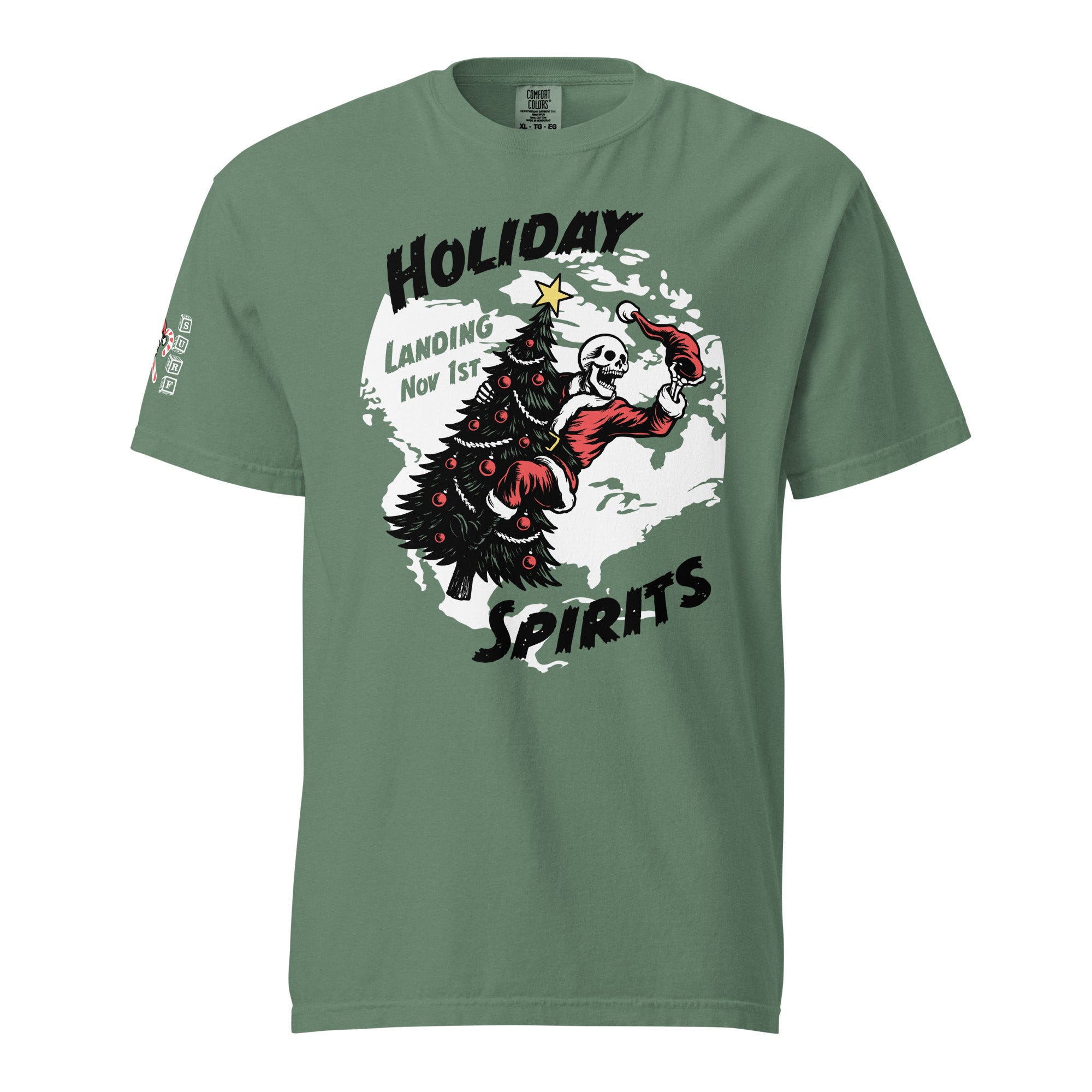 Model wearing "Holiday Spirits" front print garment-dyed heavyweight t-shirt in light green, front view featuring full color graphic of a skeleton Santa riding a decorated Christmas tree inside a white splatter map shape with arched "Holiday" and "Spirits" text and "Landing Nov 1st" – 17th & Surf