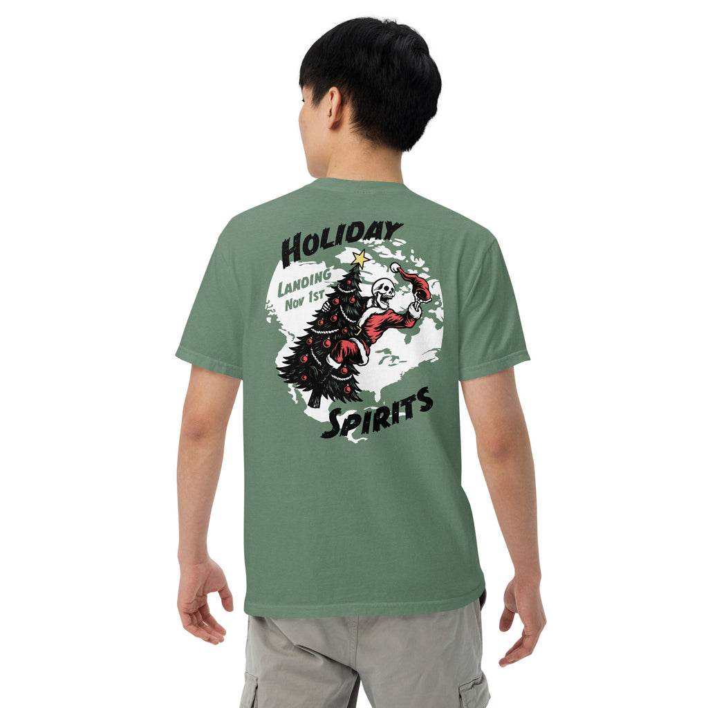 Model wearing "Holiday Spirits" garment-dyed heavyweight t-shirt in light green, back angle view featuring full color graphic of a skeleton Santa riding a decorated Christmas tree inside a white splatter map shape with arched "Holiday" and "Spirits" text and "Landing Nov 1st" – 17th & Surf