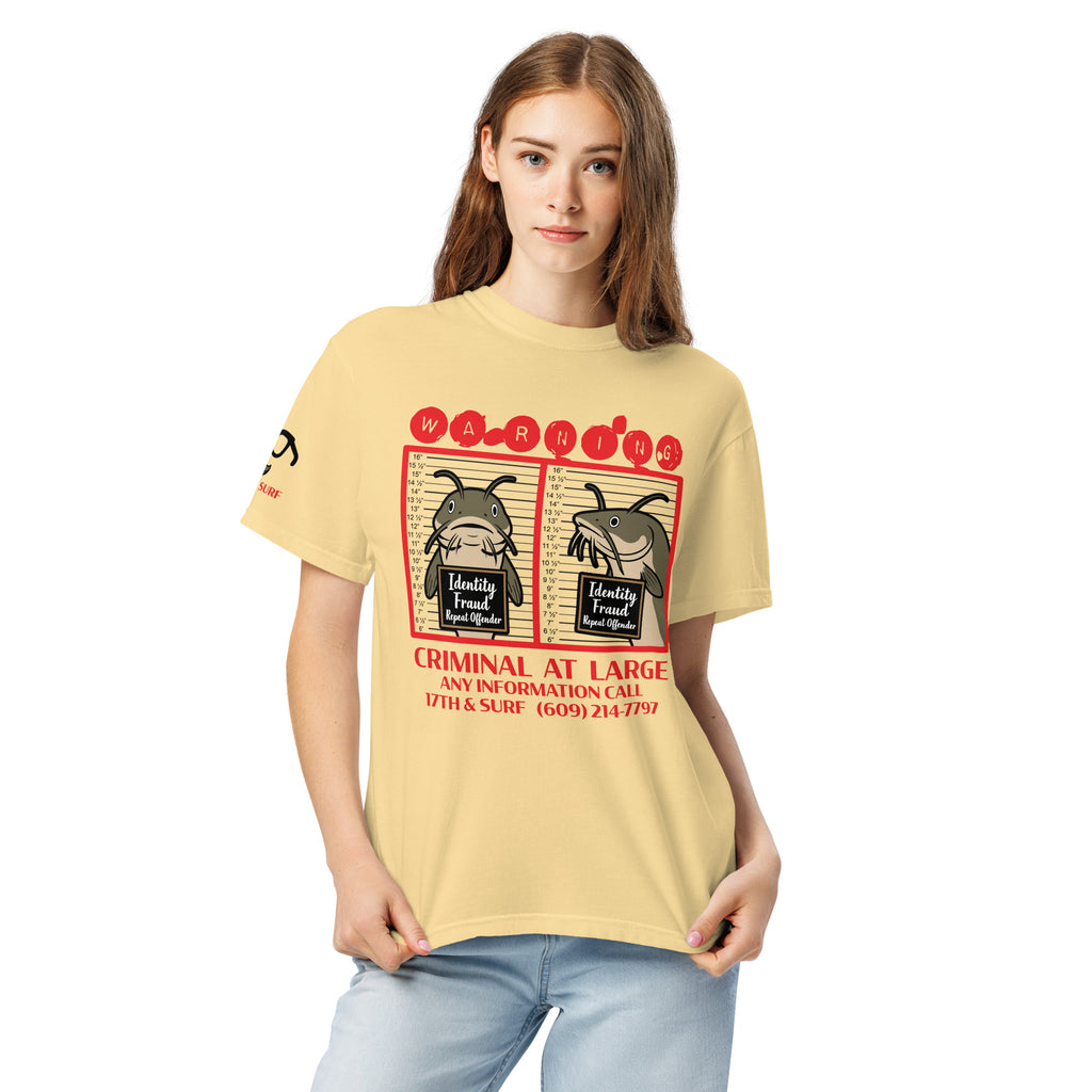 "Identity Fraud" butter garment-dyed heavyweight tee on female model, front view, featuring catfish "WARNING" mugshot graphic with "Identity Fraud, Repeat Offender" police lineup – 17th & Surf