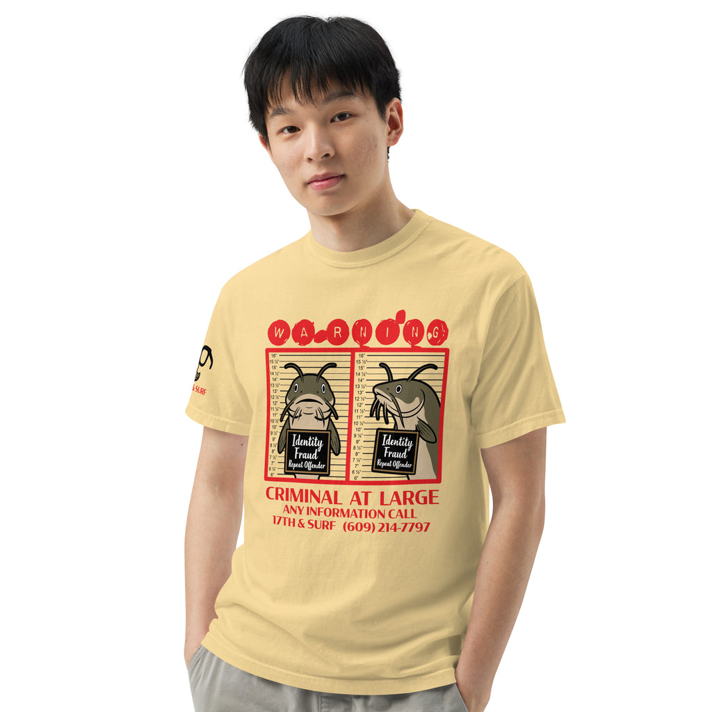 "Identity Fraud" butter garment-dyed heavyweight tee on male model, front view, featuring catfish "WARNING" mugshot graphic with "Identity Fraud, Repeat Offender" police lineup – 17th & Surf