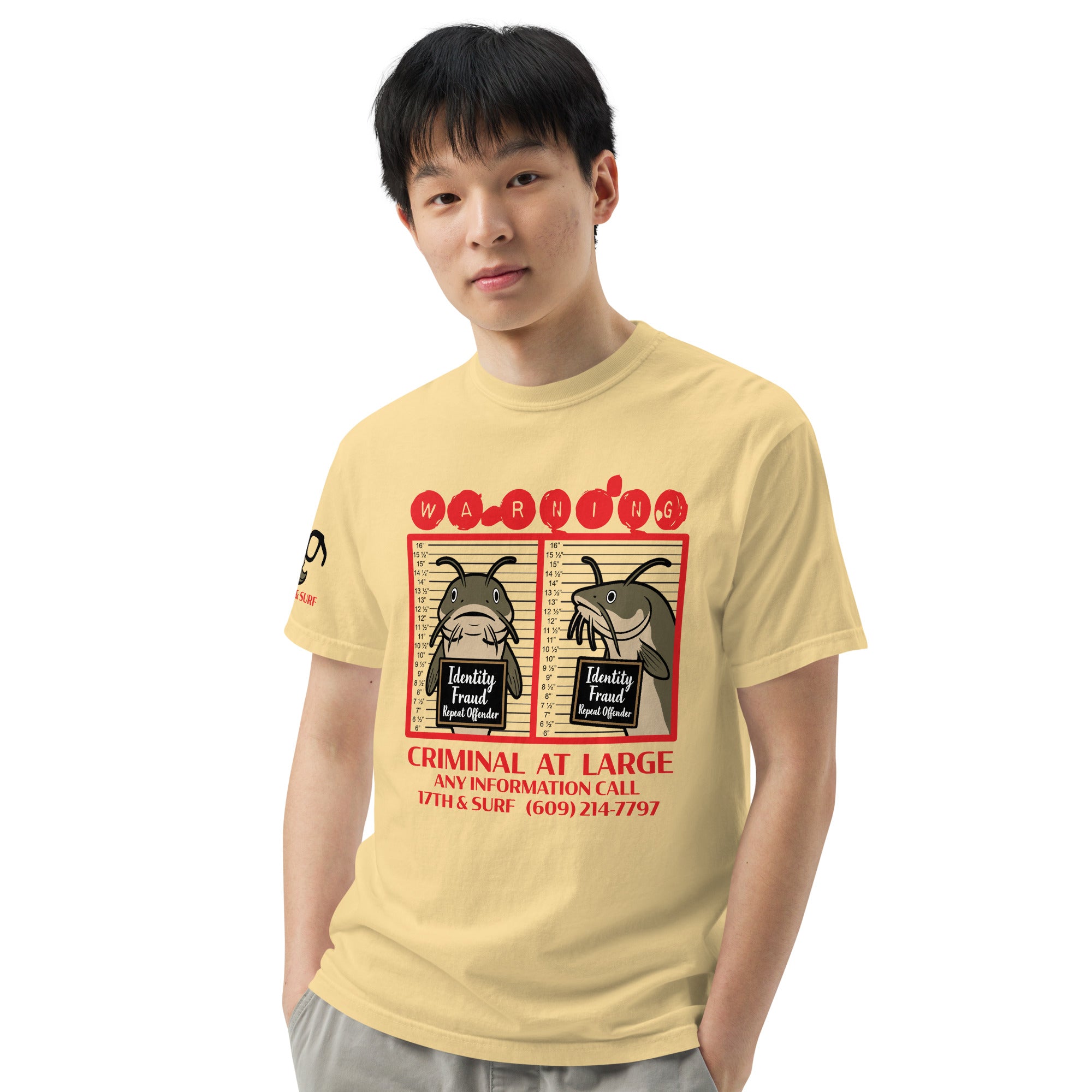 "Identity Fraud" butter garment-dyed heavyweight tee on male model, front view, featuring catfish "WARNING" mugshot graphic with "Identity Fraud, Repeat Offender" police lineup – 17th & Surf