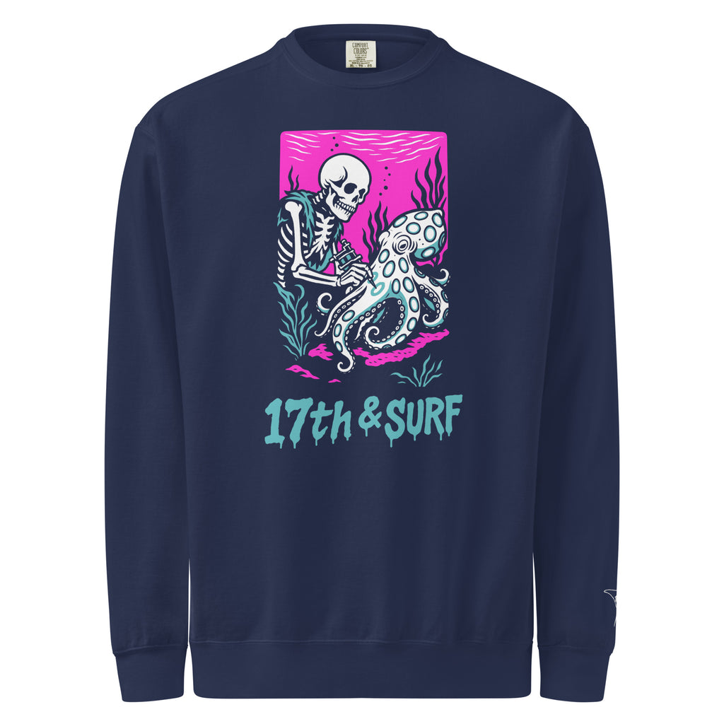 "Inked" garment-dyed heavyweight crewneck sweatshirt front view in true navy featuring skeleton tattooing an octopus graphic with "17th & Surf" text on pink background – 17th & Surf