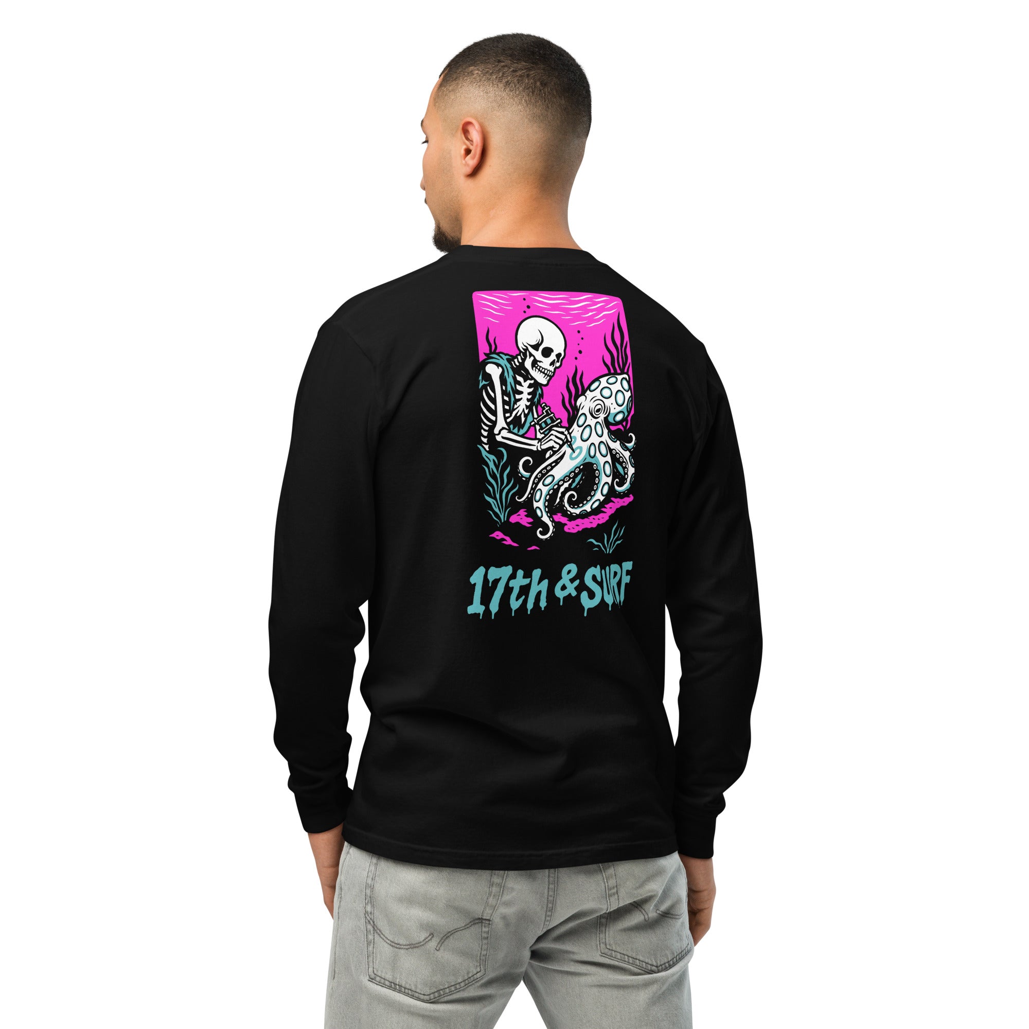 "Inked" garment-dyed heavyweight long sleeve back view in black featuring skeleton tattooing an octopus graphic with "17th & Surf" text on pink background – 17th & Surf