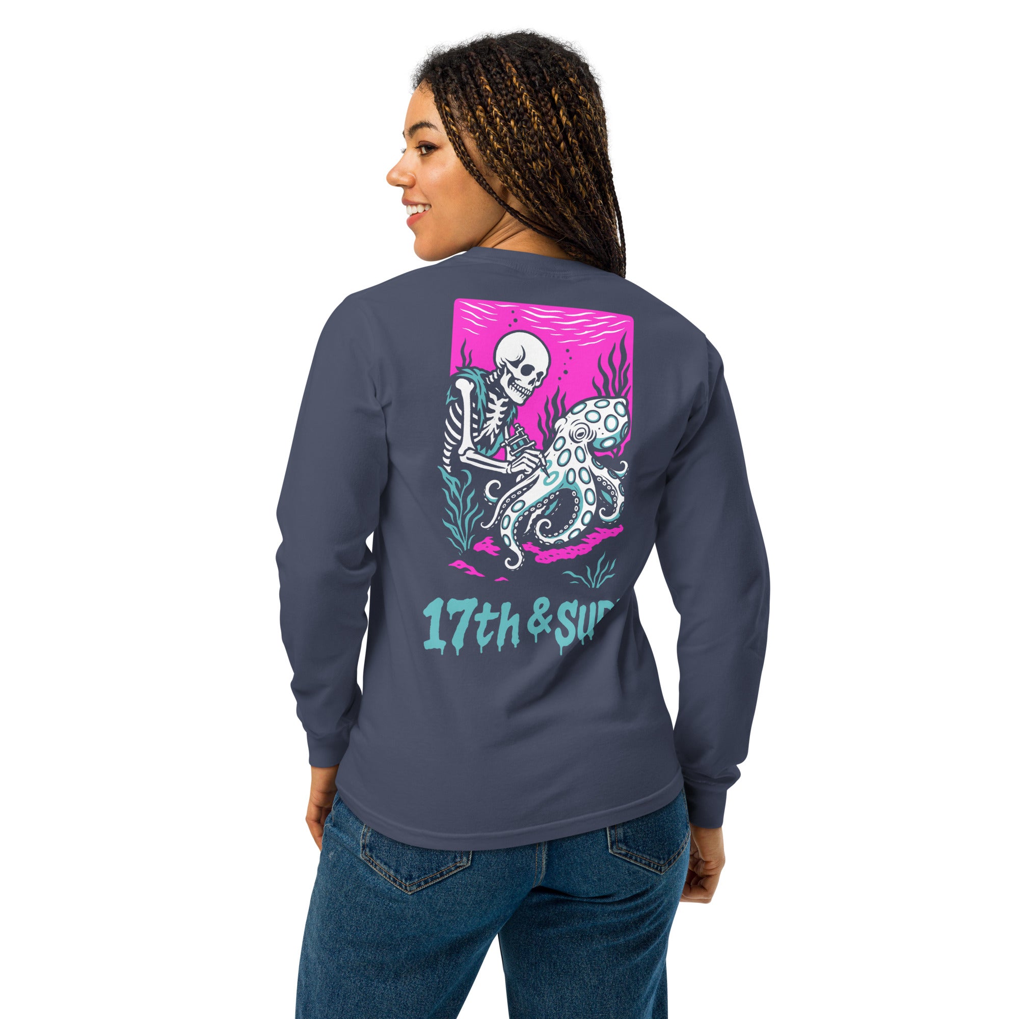"Inked" garment-dyed heavyweight long sleeve back view on model in true navy featuring skeleton tattooing an octopus graphic with "17th & Surf" text on pink background – 17th & Surf
