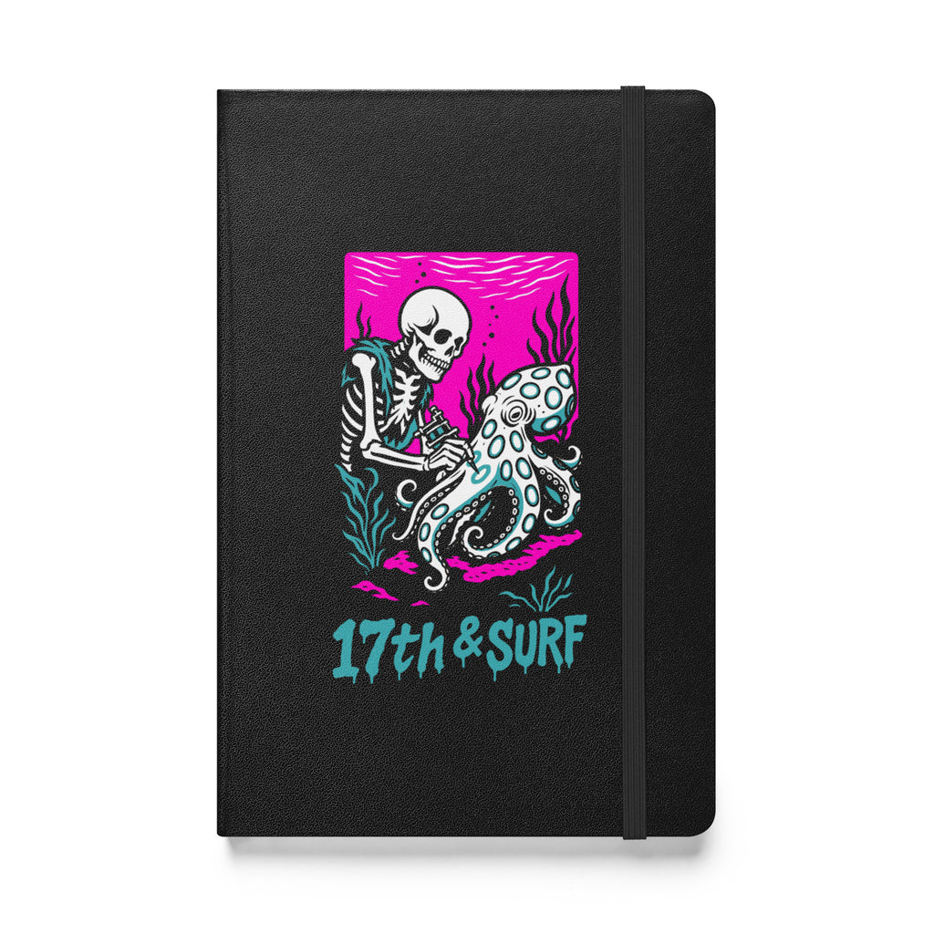 "Inked" hardcover notebook front cover in black featuring skeleton tattooing an octopus graphic with "17th & Surf" text on pink background – 17th & Surf