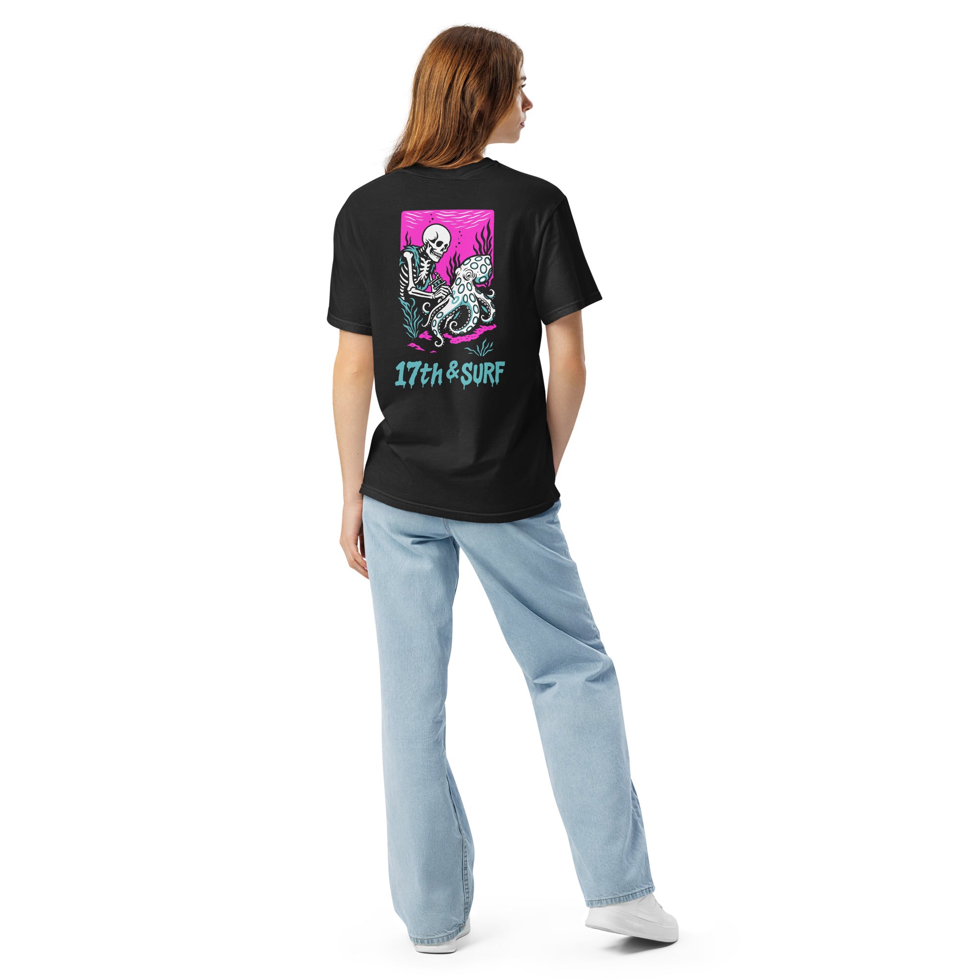 "Inked" garment-dyed heavyweight tee back view on female model in black featuring skeleton tattooing an octopus graphic with "17th & Surf" text on pink background – 17th & Surf