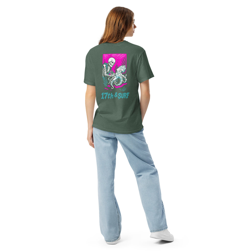 "Inked" garment-dyed heavyweight tee back view in blue spruce featuring skeleton tattooing an octopus graphic with "17th & Surf" text on pink background – 17th & Surf