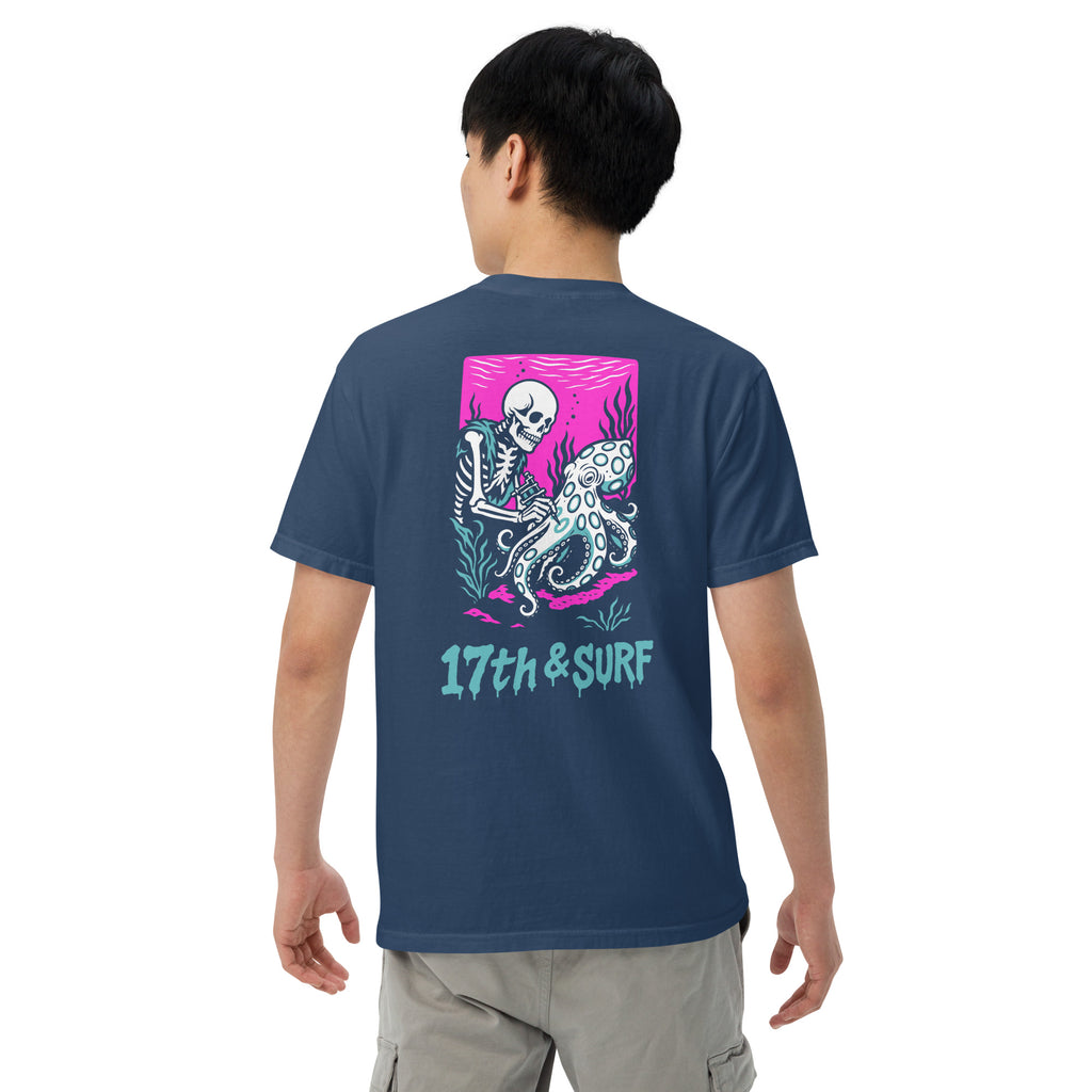 "Inked" garment-dyed heavyweight tee back view on male model in true navy featuring skeleton tattooing an octopus graphic with "17th & Surf" text on pink background – 17th & Surf