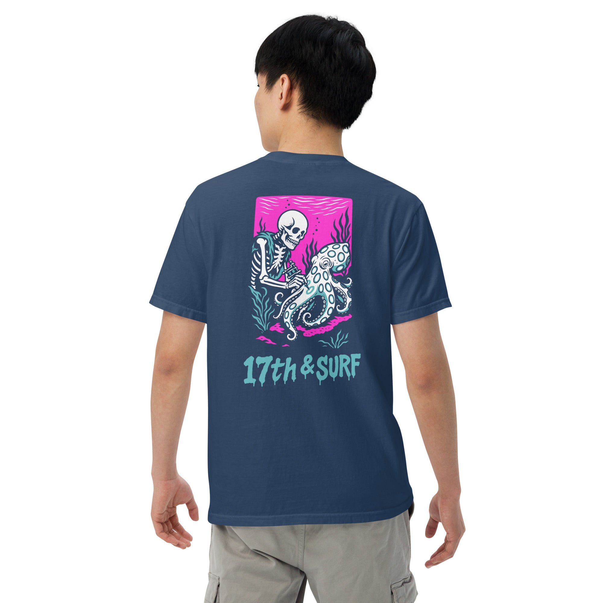 "Inked" garment-dyed heavyweight tee back view on male model in true navy featuring skeleton tattooing an octopus graphic with "17th & Surf" text on pink background – 17th & Surf