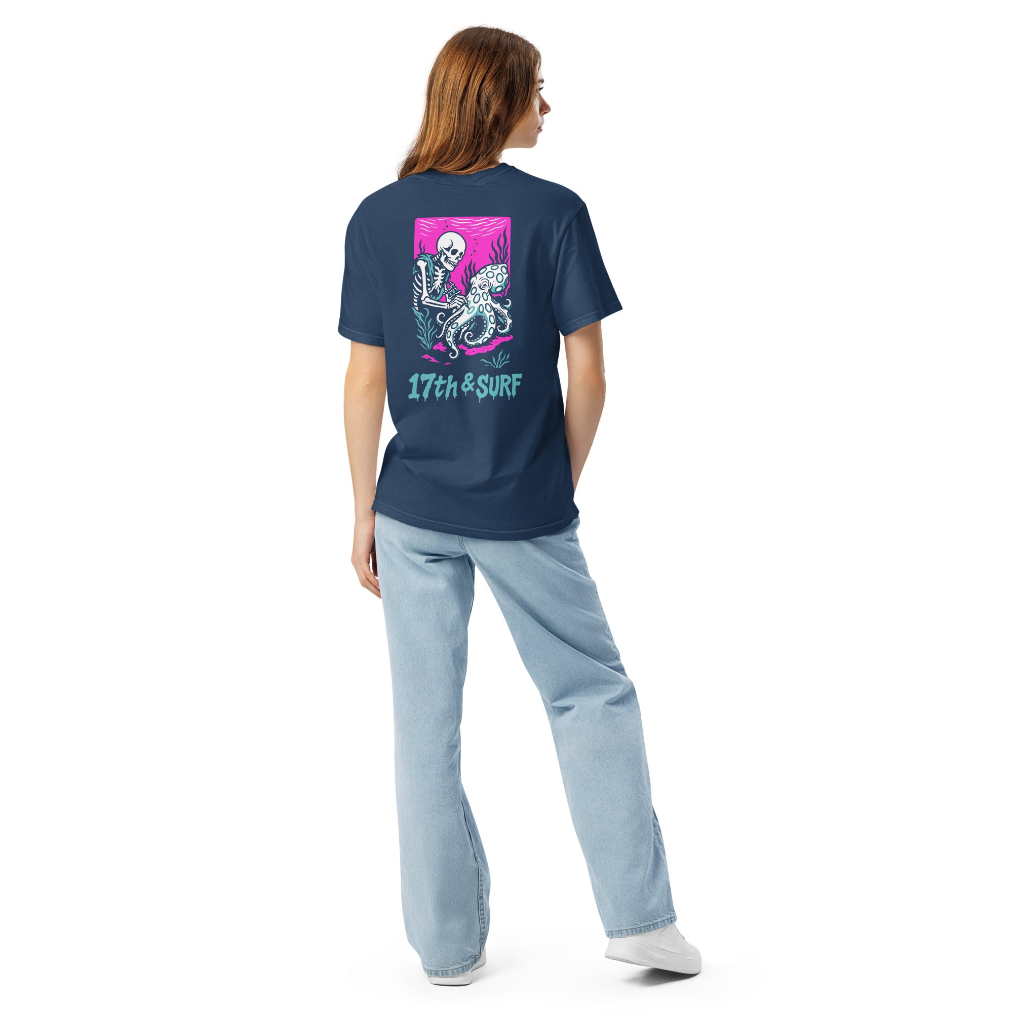 "Inked" garment-dyed heavyweight tee back view on female model in true navy featuring skeleton tattooing an octopus graphic with "17th & Surf" text on pink background – 17th & Surf