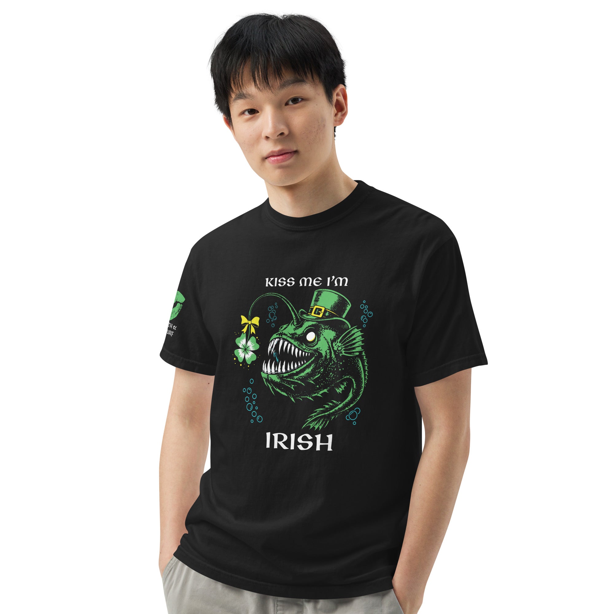 "Kiss Me I'm Irish" Anglerfish black tee on male model, front view, featuring the green leprechaun anglerfish with shamrock lure and "KISS ME I'M IRISH" text, plus a dripping-lips "17TH & SURF" sleeve logo – 17th & Surf