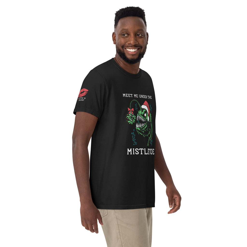 "Mistletoe" Anglerfish black heavyweight t-shirt on male model, 3/4 angle view, featuring a green anglerfish wearing a Santa hat with mistletoe and "Meet Me Under The Mistletoe" graphic – 17th & Surf