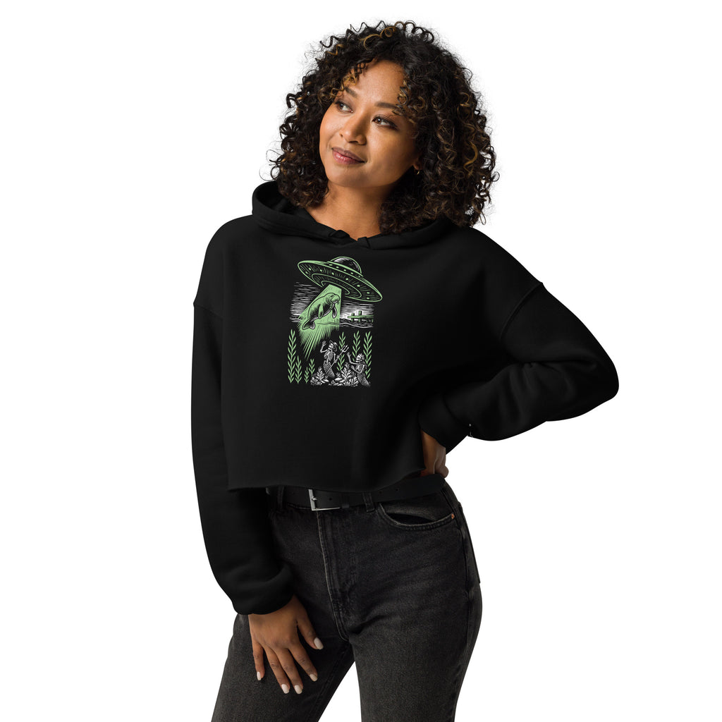 "Ocean Abduction" women's cropped hoodie, front angle on model, featuring UFO abducting a manatee via tractor beam over skeleton mermaids design – 17th & Surf