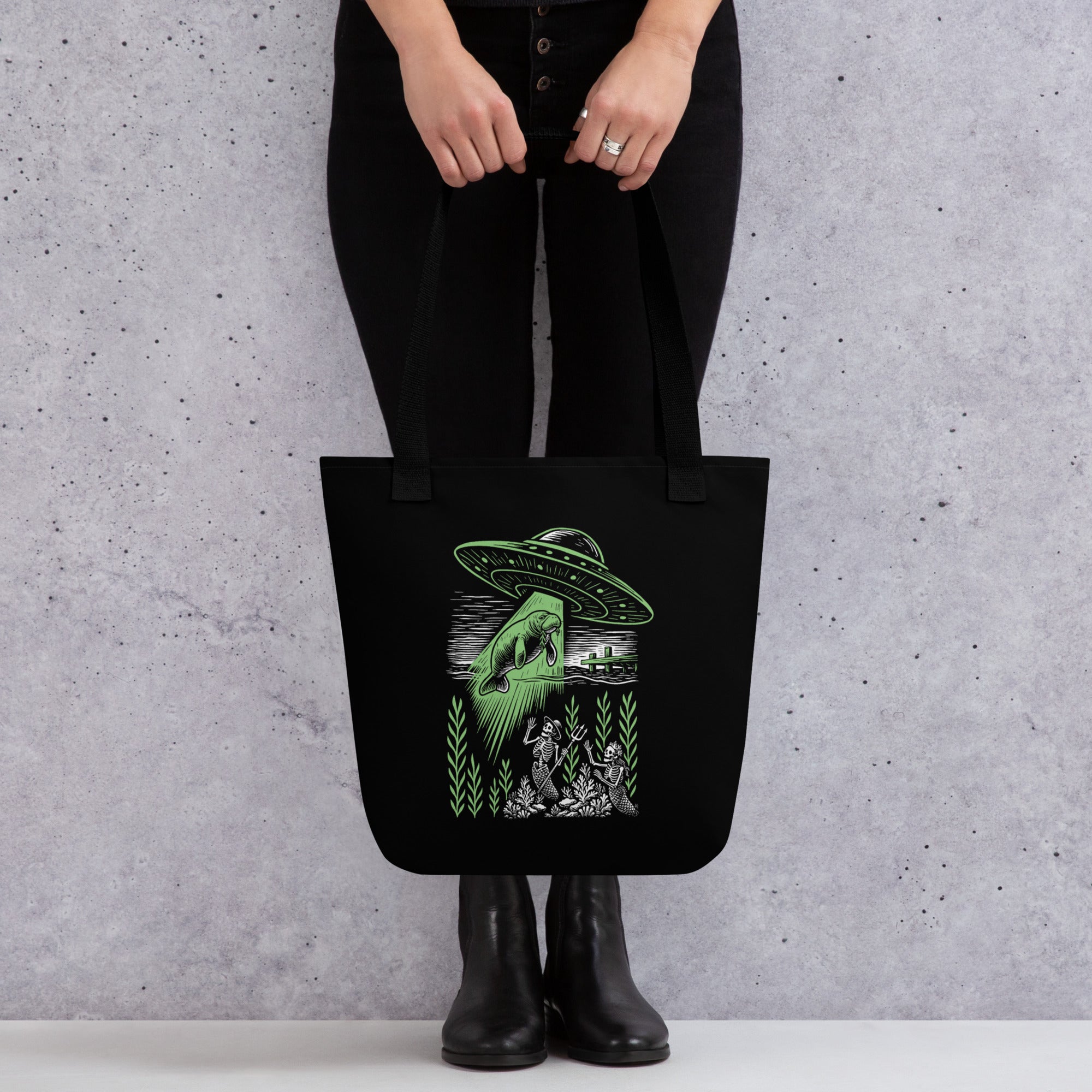 "Ocean Abduction" canvas tote bag on model, featuring UFO abducting a manatee via tractor beam over skeleton mermaids design – 17th & Surf