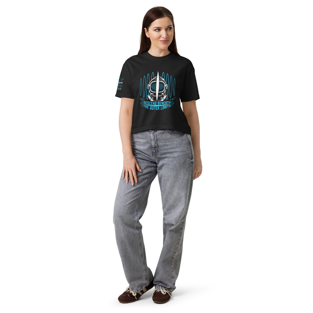 "Beneath The Outer Limits" women's heavyweight boxy tee in black, front view on female model, featuring the large front-chest graphic of a vintage diving helmet split by a surfboard fin, framed by blue broadcast test-pattern rings, with the text "DESCEND BENEATH THE OUTER LIMITS" – "Beneath The Outer Limits" Series by 17th & Surf