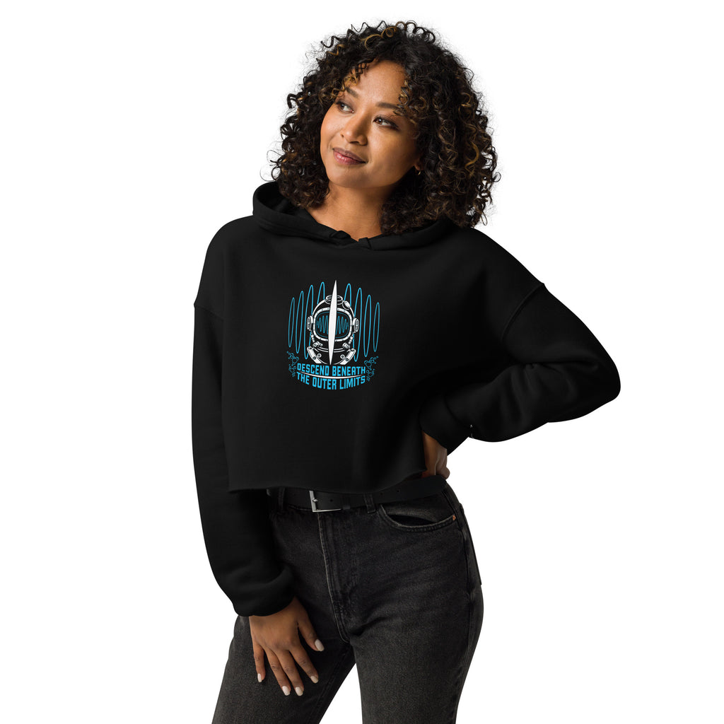 "Beneath The Outer Limits" women's cropped hoodie in black, front view on female model, featuring the large graphic of a vintage diving helmet split by a surfboard fin, framed by blue broadcast test-pattern rings, with the text "DESCEND BENEATH THE OUTER LIMITS" – "Beneath The Outer Limits" Series by 17th & Surf