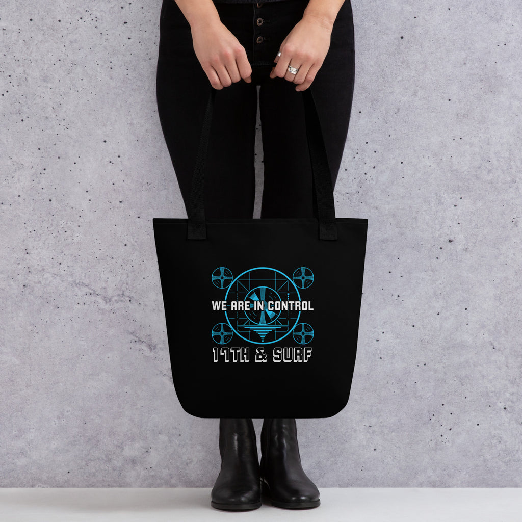 "Beneath The Outer Limits" black all-over print tote bag, back view on female model, featuring the small blue "WE ARE IN CONTROL" broadcast test-pattern logo with "17th & Surf" text – "Beneath The Outer Limits" Series by 17th & Surf