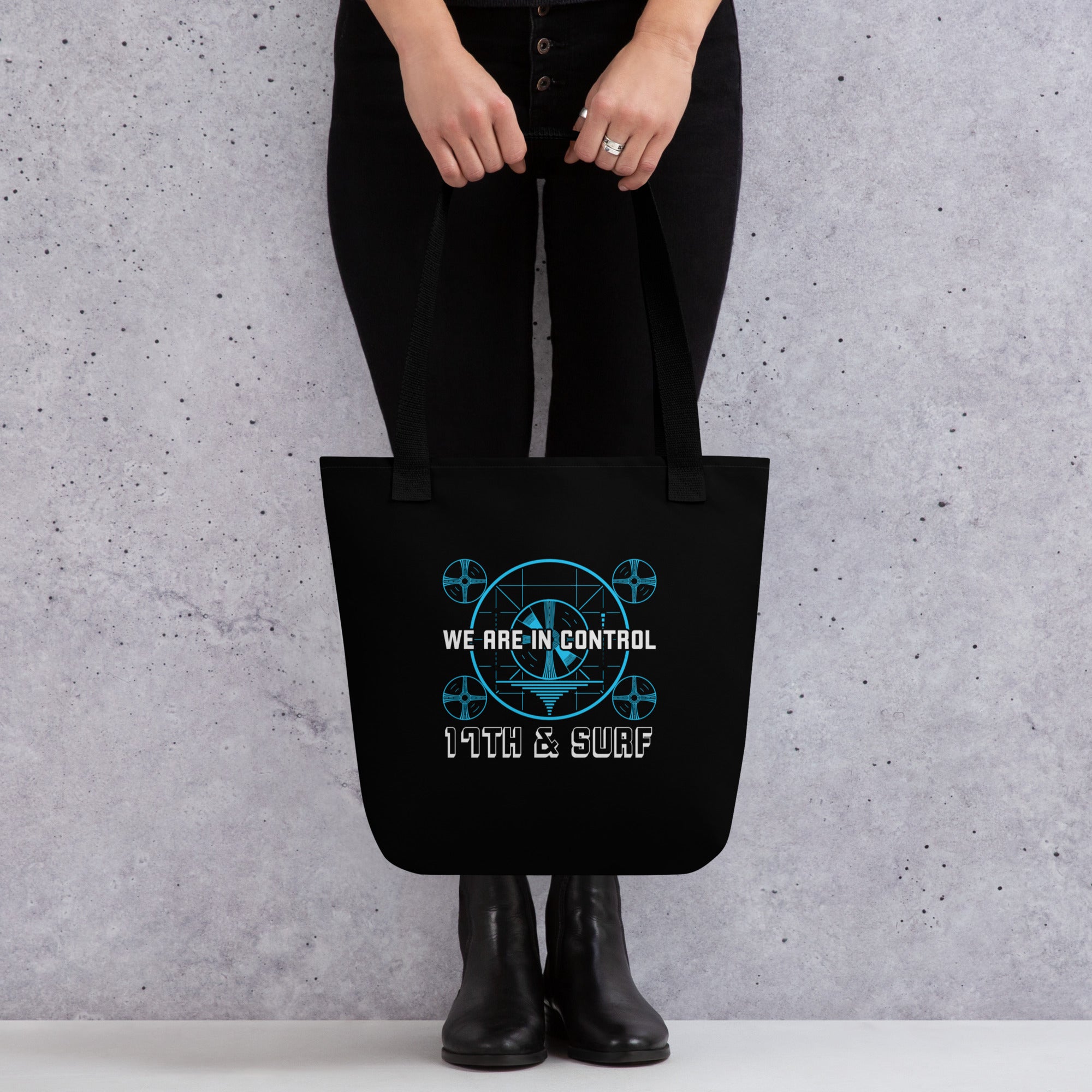 "Beneath The Outer Limits" black all-over print tote bag, back view on female model, featuring the small blue "WE ARE IN CONTROL" broadcast test-pattern logo with "17th & Surf" text – "Beneath The Outer Limits" Series by 17th & Surf