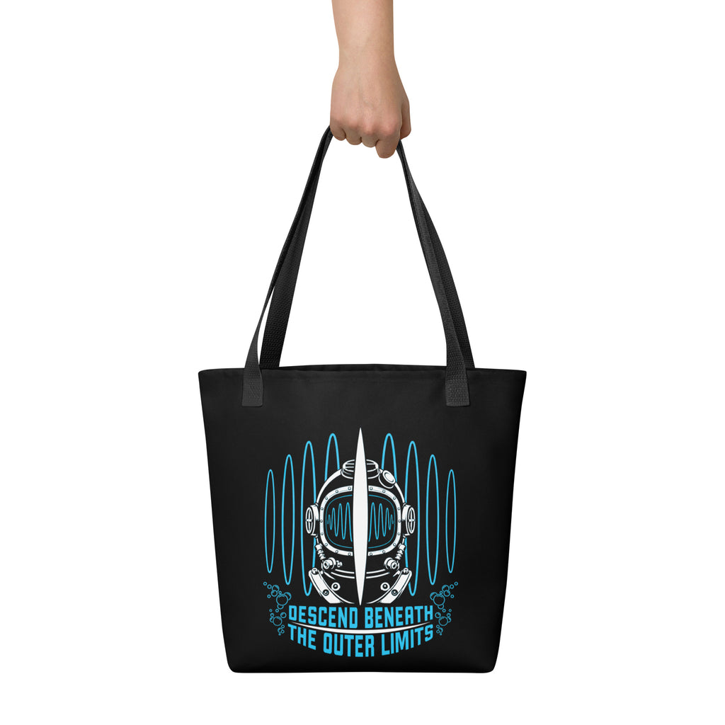 "Beneath The Outer Limits" black all-over print tote bag, held by hand, featuring the large graphic of a vintage diving helmet split by a surfboard fin, framed by blue broadcast test-pattern rings with an oscillating waveform, rising bubbles, and the text "DESCEND BENEATH THE OUTER LIMITS" – "Beneath The Outer Limits" Series by 17th & Surf