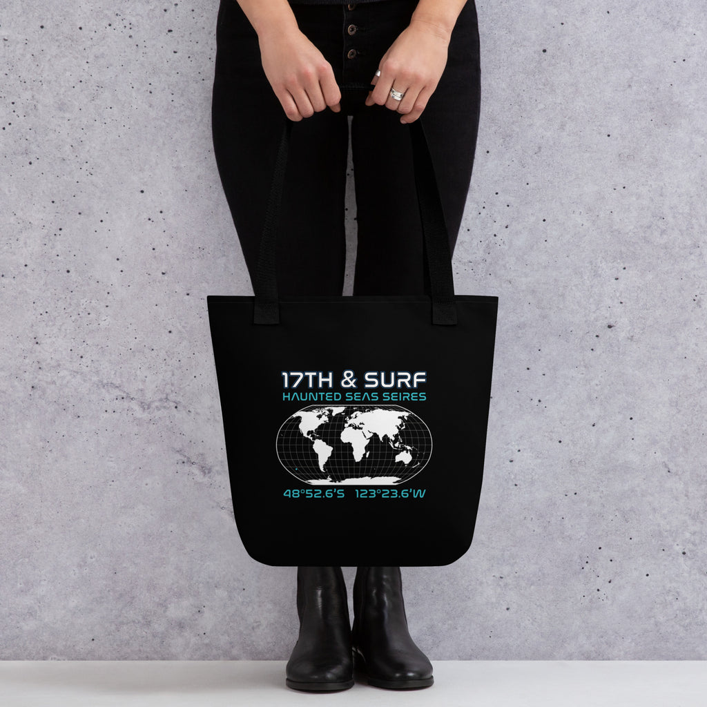 "Point Nemo" black canvas tote bag, back view on model, featuring the Haunted Seas Series world map patch with coordinates 48°52.6'S 123°23.6'W – "Haunted Seas" Series by 17th & Surf