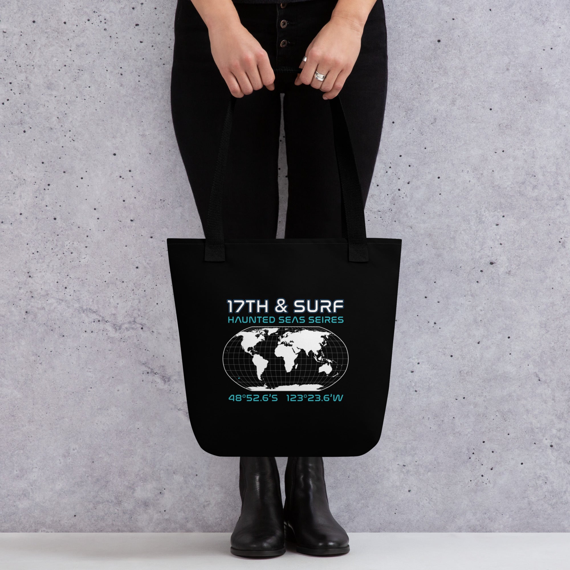 "Point Nemo" black canvas tote bag, back view on model, featuring the Haunted Seas Series world map patch with coordinates 48°52.6'S 123°23.6'W – "Haunted Seas" Series by 17th & Surf