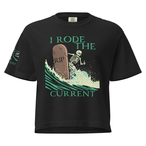 "RIP Current" women's heavyweight boxy tee in black, front view showing skeleton surfing a "RIP" tombstone "I Rode the Current" graphic and "17TH & SURF" sleeve emblem – 17th & Surf